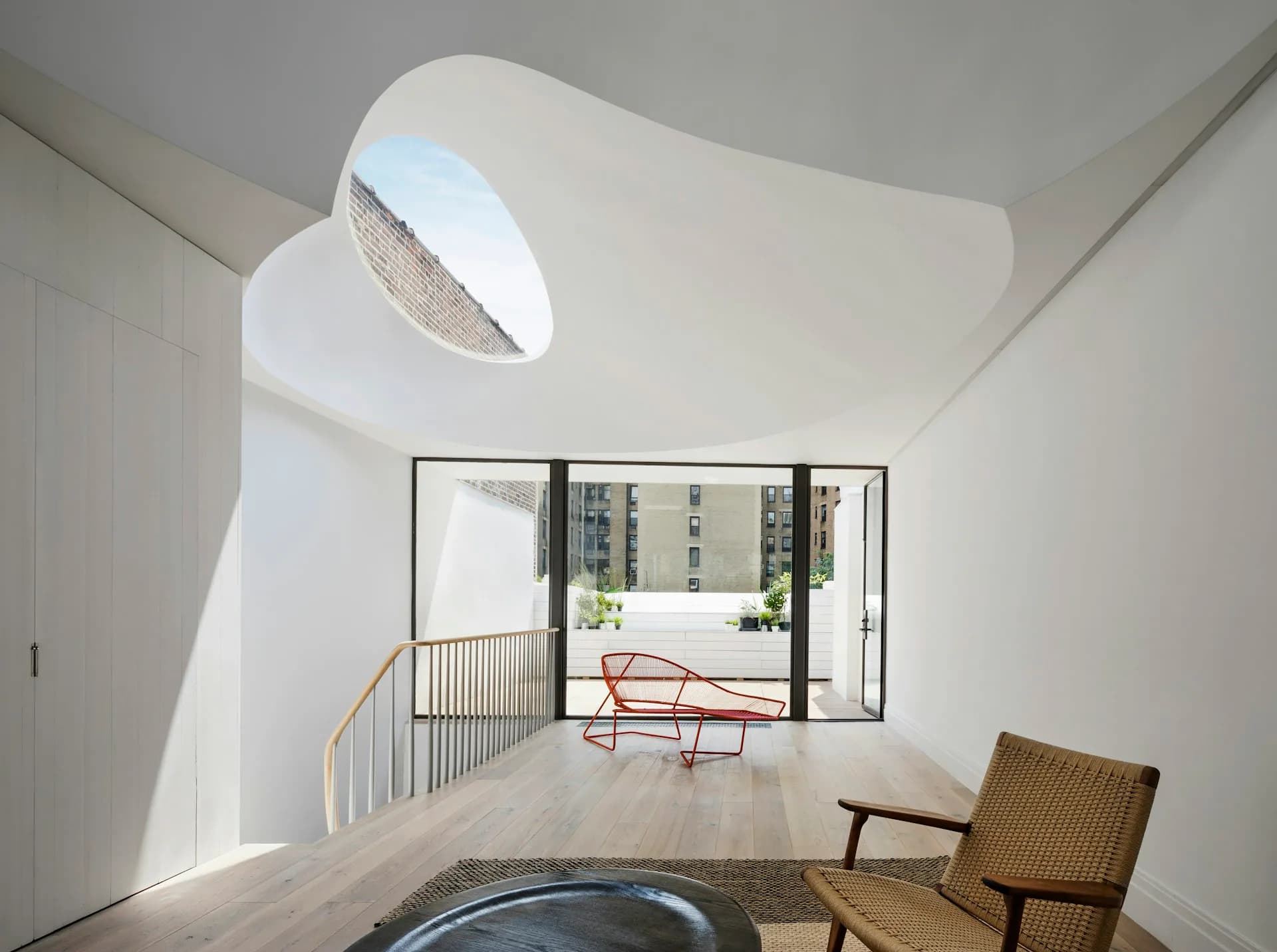 Bright minimalist loft with curved white walls, sculptural skylight, wooden flooring, and mid-century furniture overlooking a balcony by O'Neill Rose Architects.
