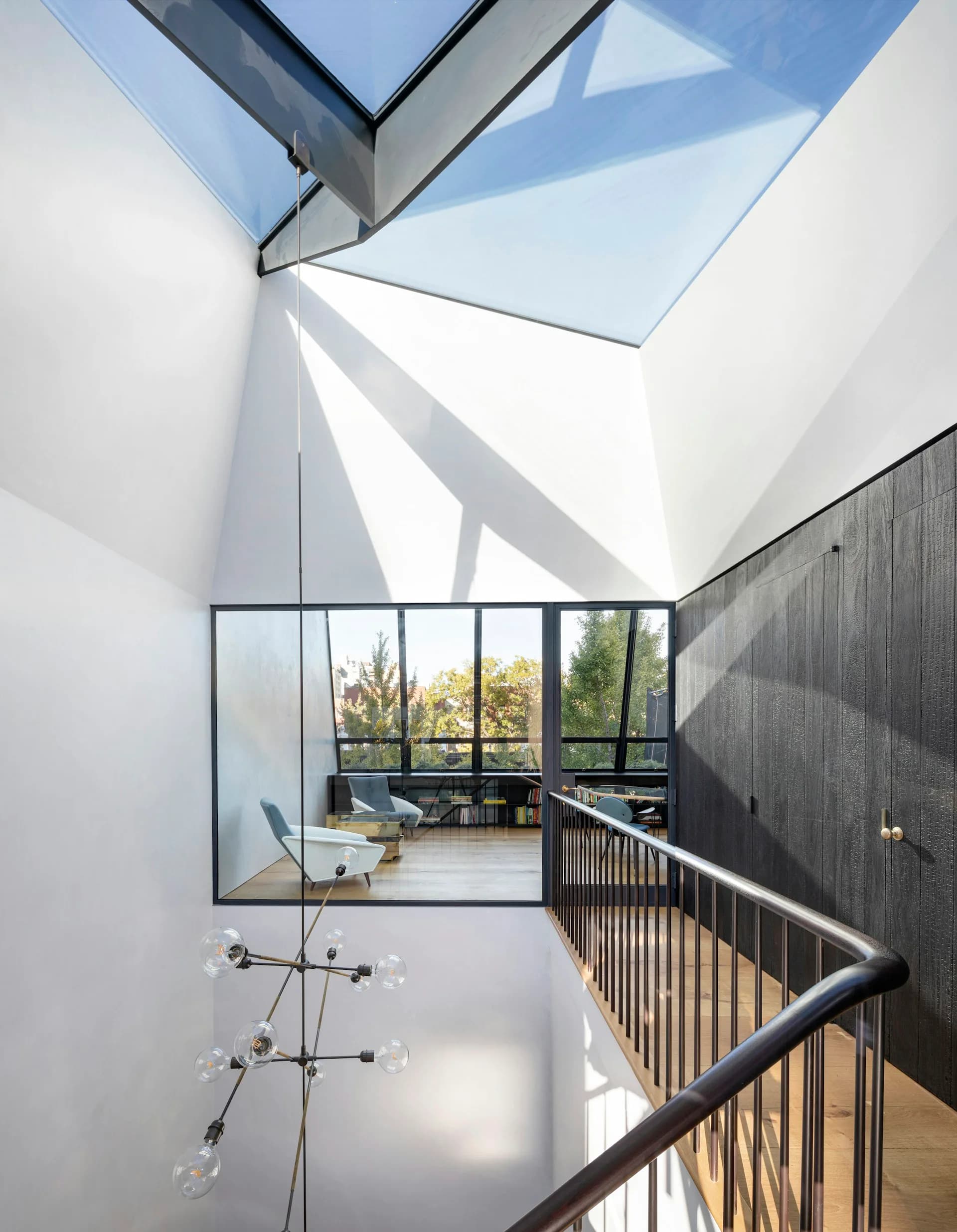 Multi-story interior with skylight, white walls, black metal railings, and large framed windows overlooking greenery by O'Neill Rose Architects.
