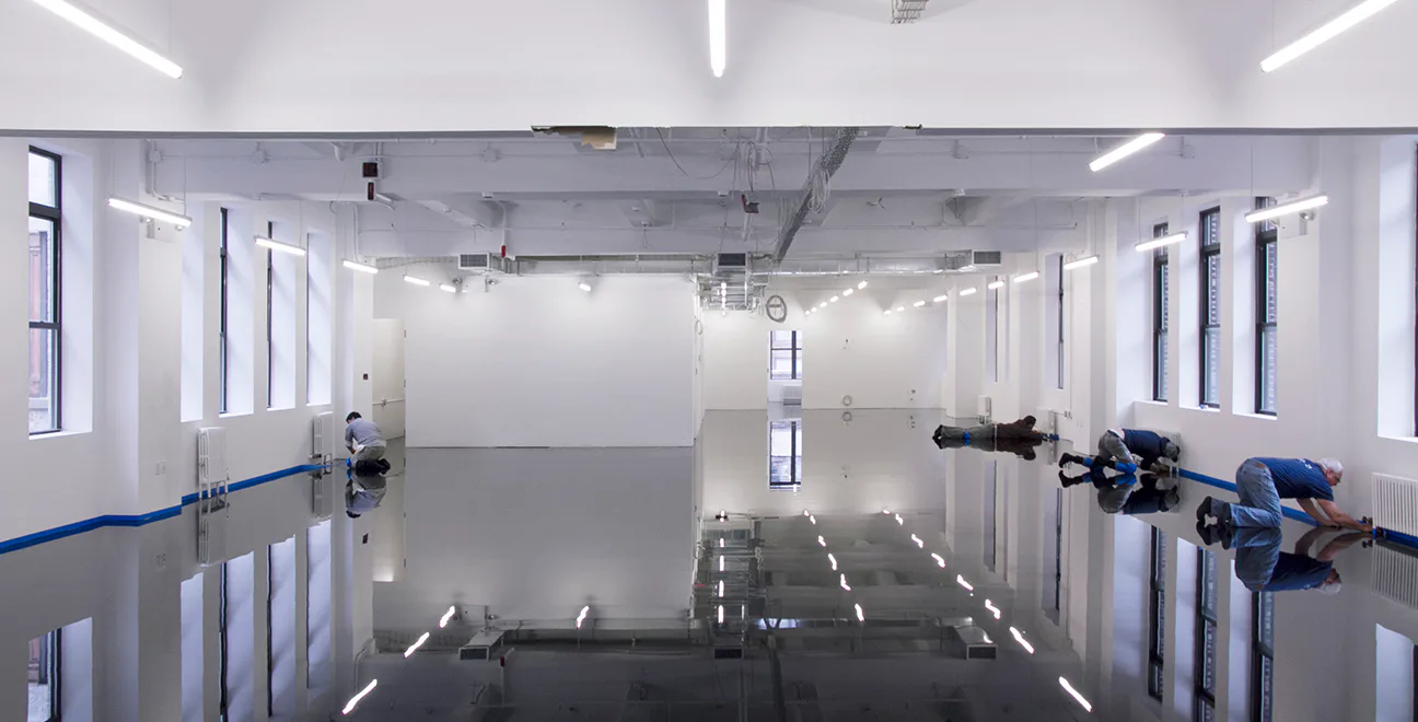 Symmetrical industrial garage interior with polished black floors, white walls, fluorescent ceiling lights, and blue equipment on either side, by Only If.
