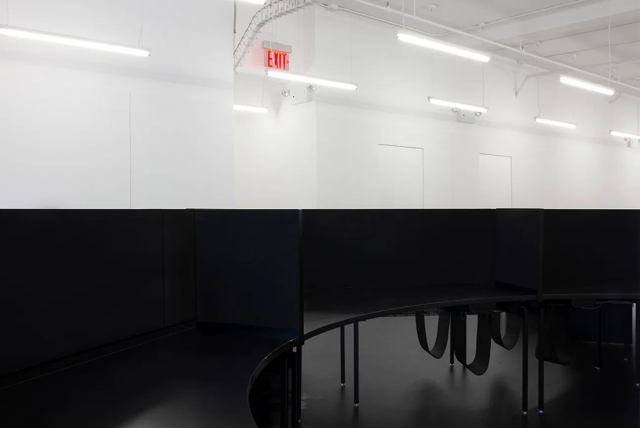 Minimalist interior space with white upper walls, black lower half, fluorescent lighting, exit sign, and dark table visible—a stark modern design by Only If.