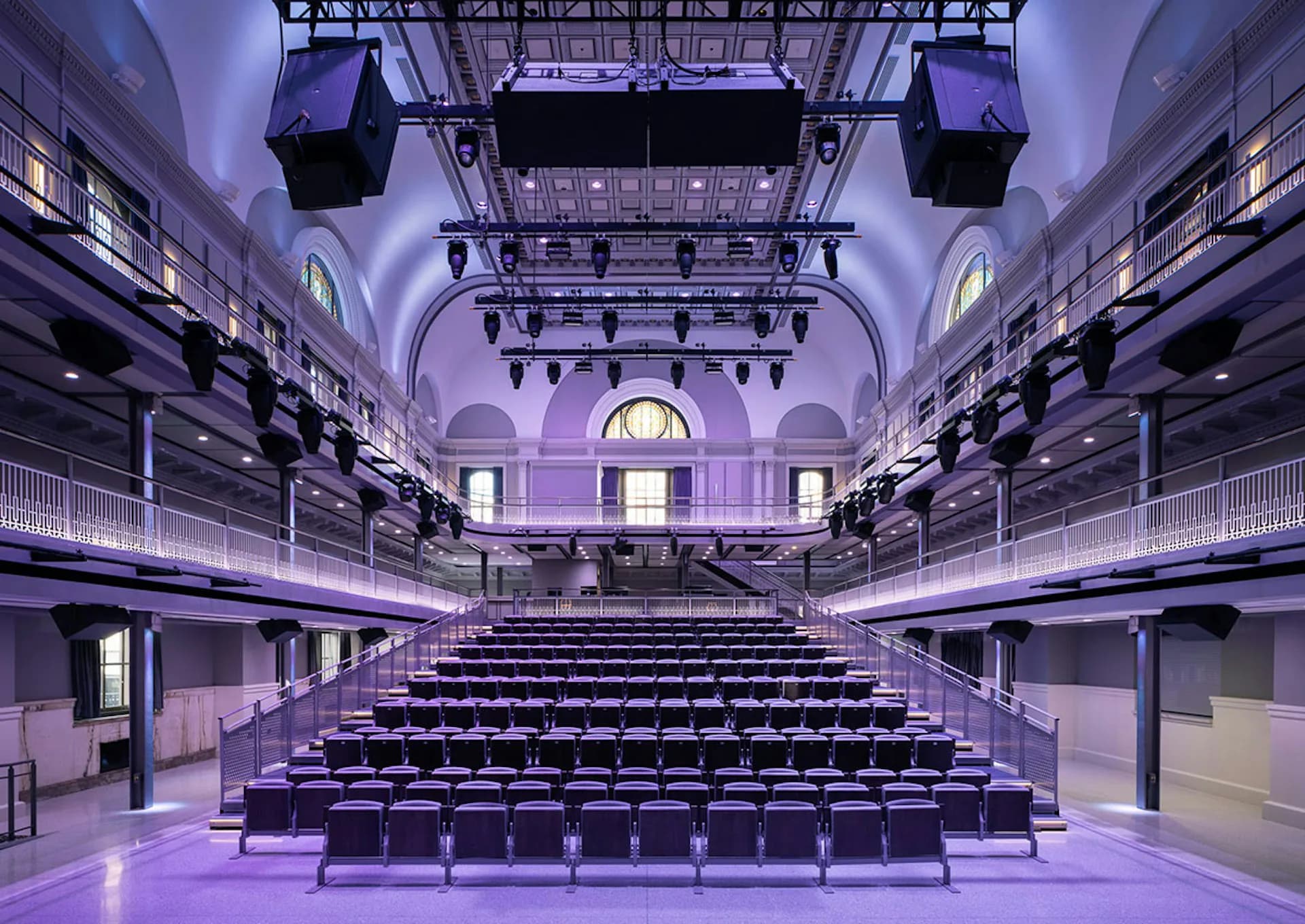 Purple-toned auditorium interior with symmetrical seating, balcony levels, and theatrical lighting by OTJ Architects.
