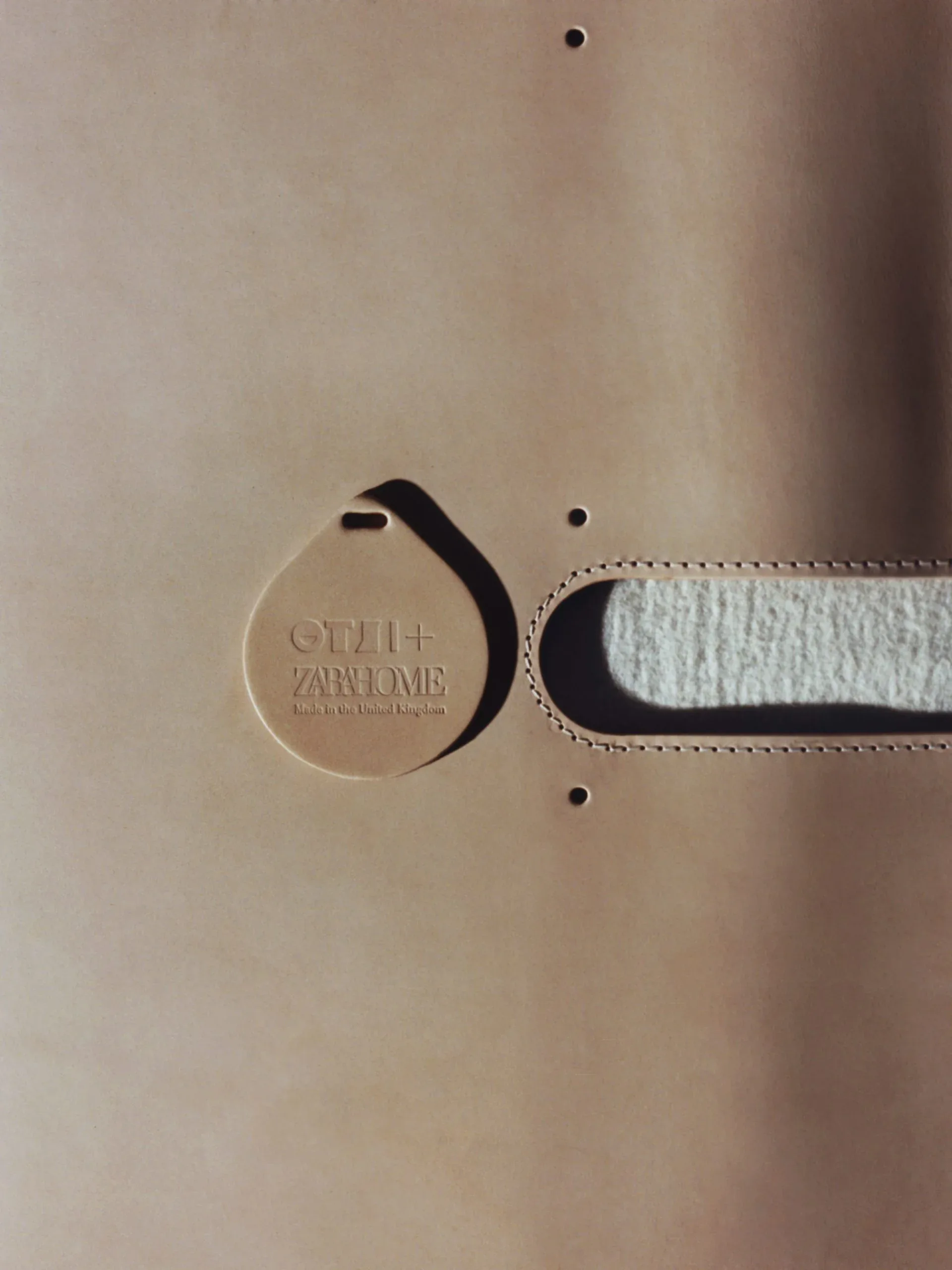 Beige leather circular tag with embossed text attached to a cream linen belt with decorative stitching, showcasing branding detail by Otzi.