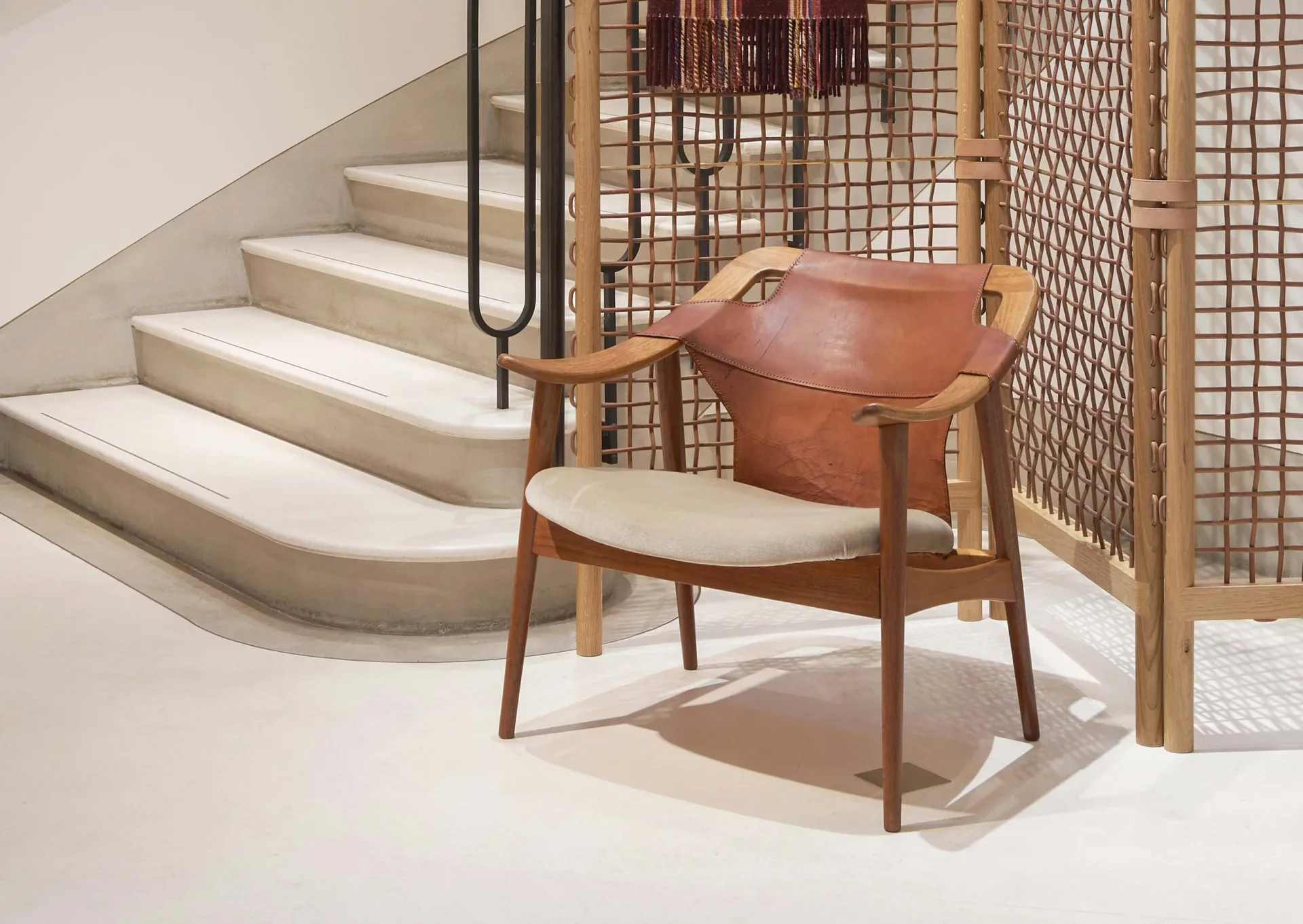 Mid-century modern interior with curved concrete staircase, wooden chair with cognac leather, and wooden room divider, designed by Otzi.