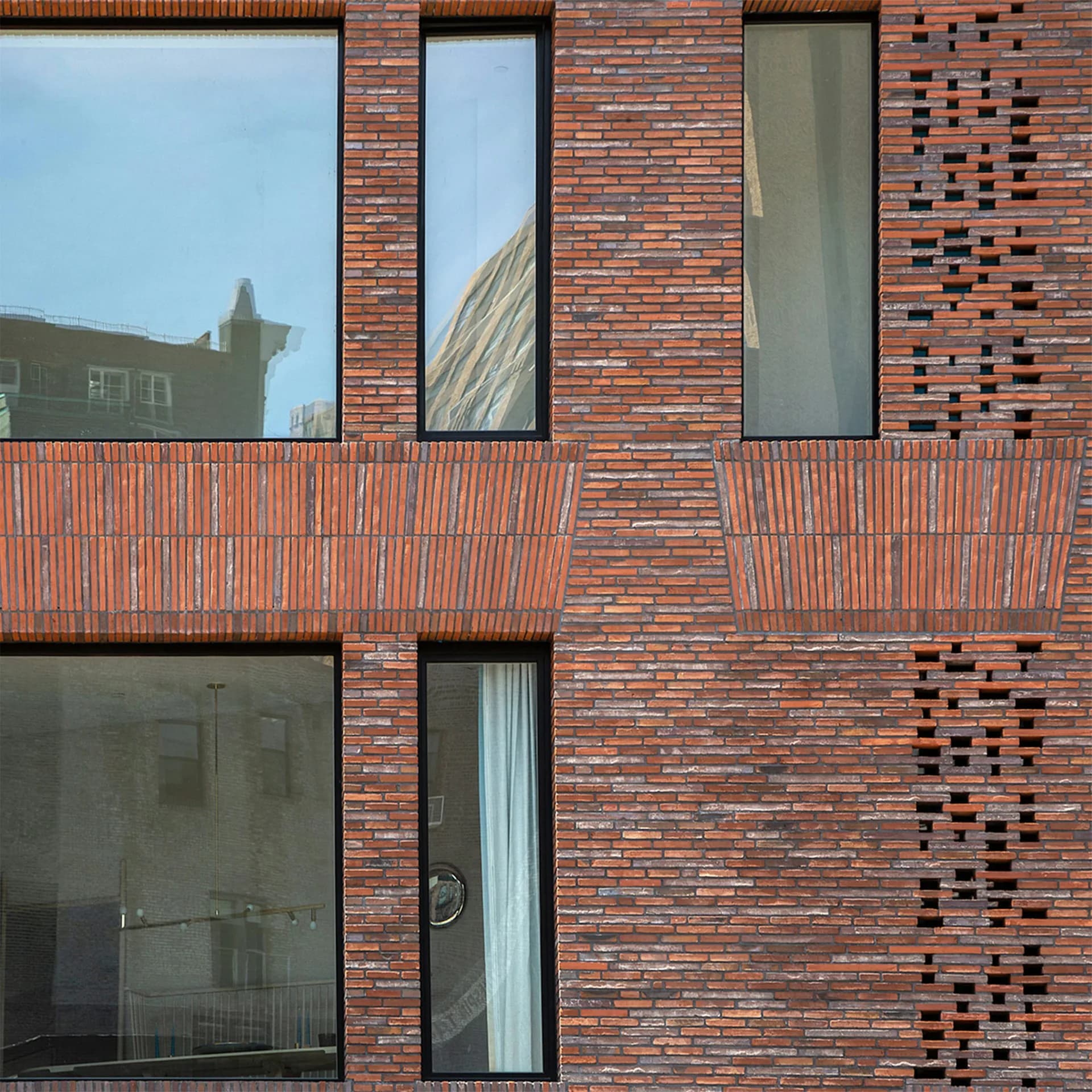 Modern brick facade with geometric window patterns, metal balconies, and dark glass elements, exemplifying contemporary architectural design by Palette Architecture.