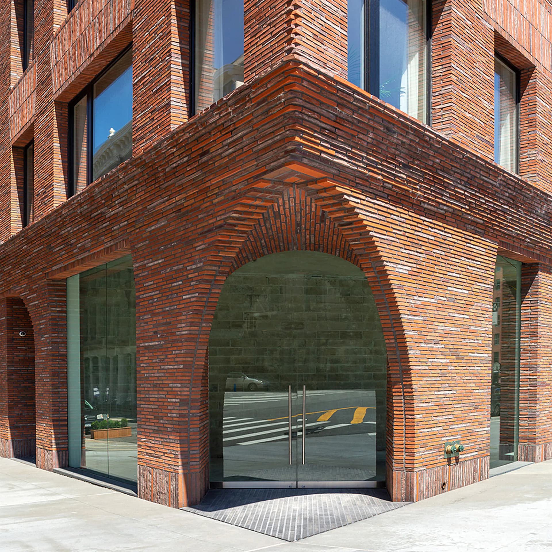Red brick corner entrance with arched opening, glass doors, and upper-story windows by Palette Architecture.