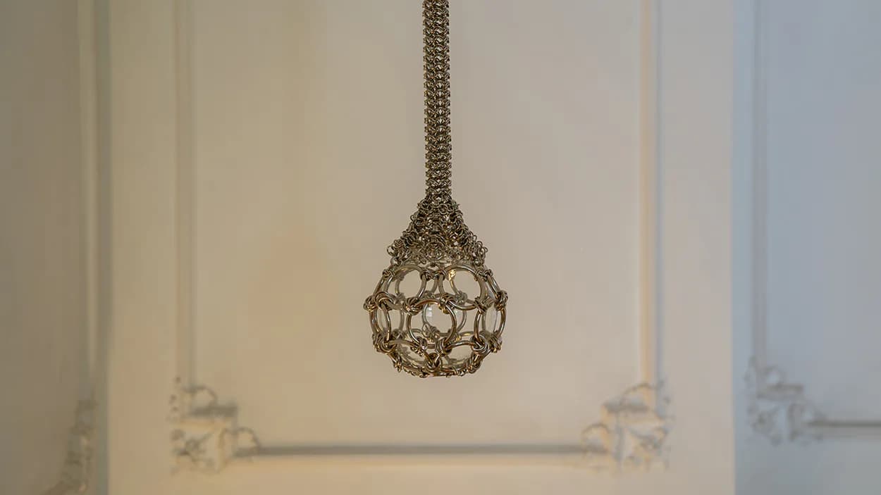 Pendant light fixture with intricate geometric wire-frame design suspended in minimalist white space by Panorammma.