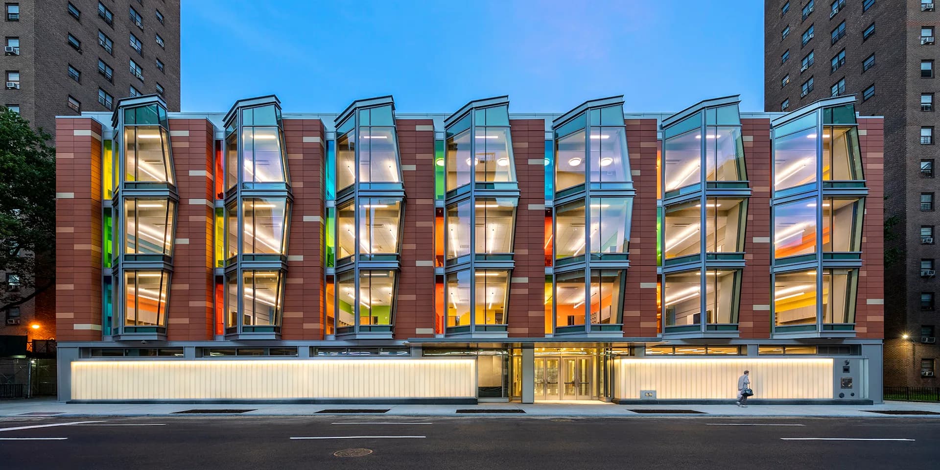 Illuminated modern storefront with colorful stacked window boxes and warm interior lighting in urban setting by PBDW Architects.