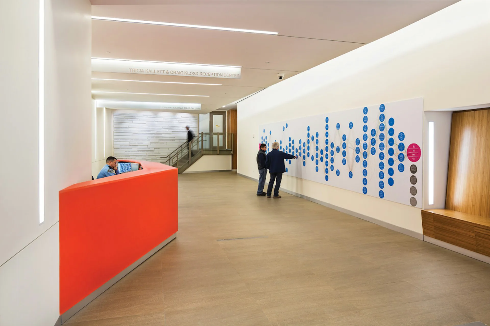 Modern office lobby with orange reception desk, linear ceiling lights, and blue circular wall installation by PBDW Architects.
