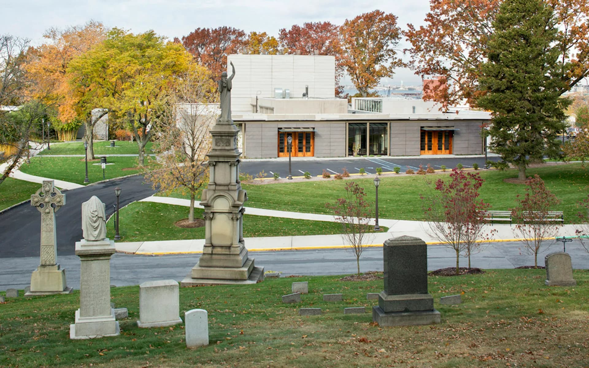 Modern residential building with clean lines and large windows overlooking a pond, surrounded by autumn trees and a cemetery, designed by PBDW Architects.