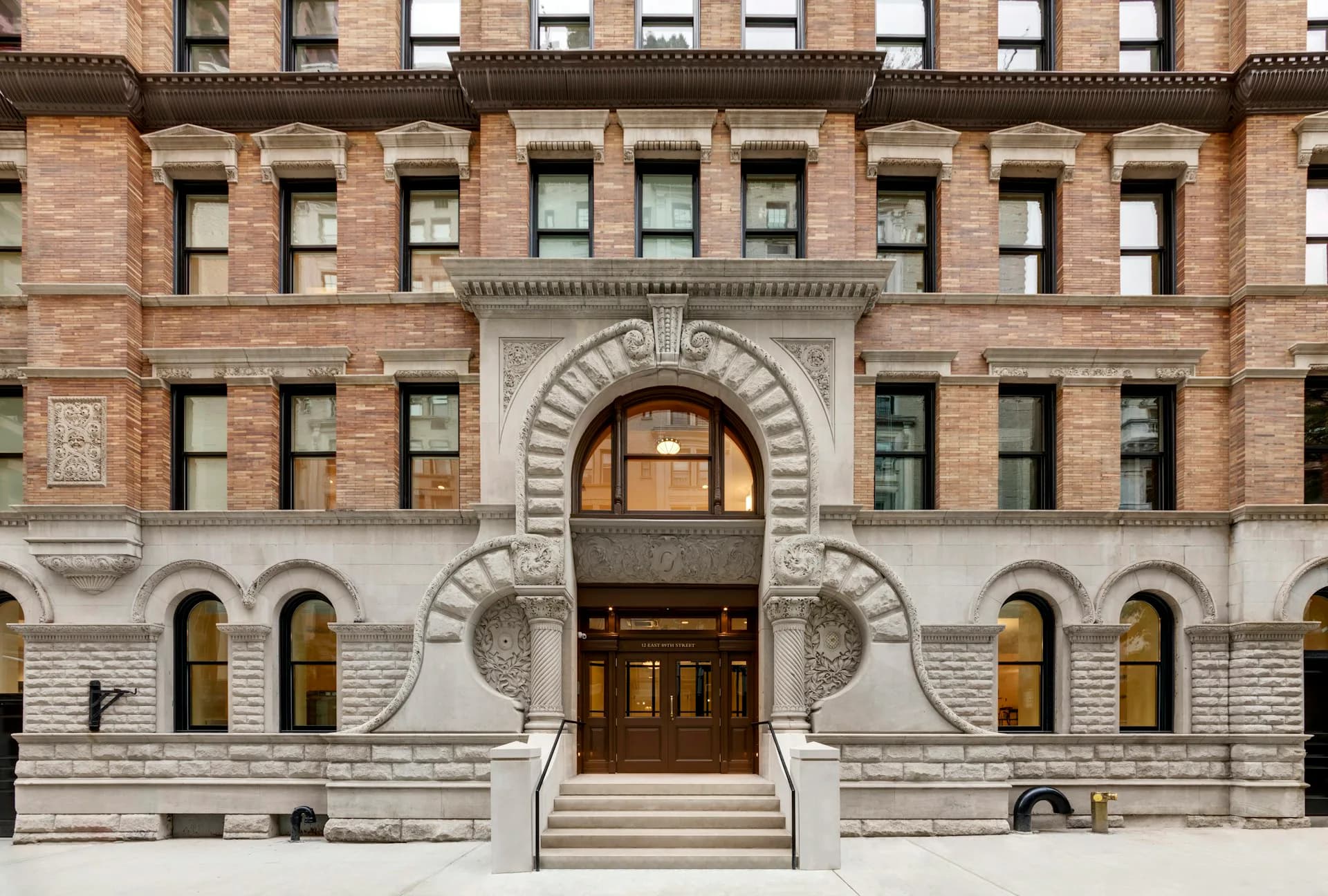 Neoclassical building facade with ornate arched entrance, red brick upper stories, and limestone base featuring symmetrical windows by PBDW Architects.