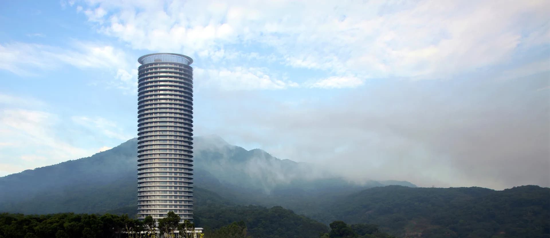 Cylindrical high-rise residential tower with horizontal striping set against misty mountains, a CGI rendering by Pei Cobb Freed & Partners Architects LLP.