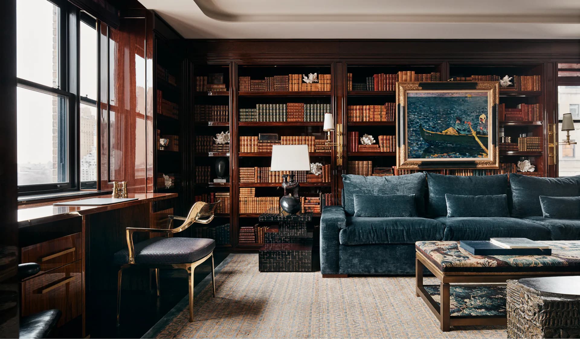 Sophisticated library lounge featuring dark wood built-in shelving, teal upholstered sofa, brass accents, and natural light from large windows, designed by Pembrooke & Ives.