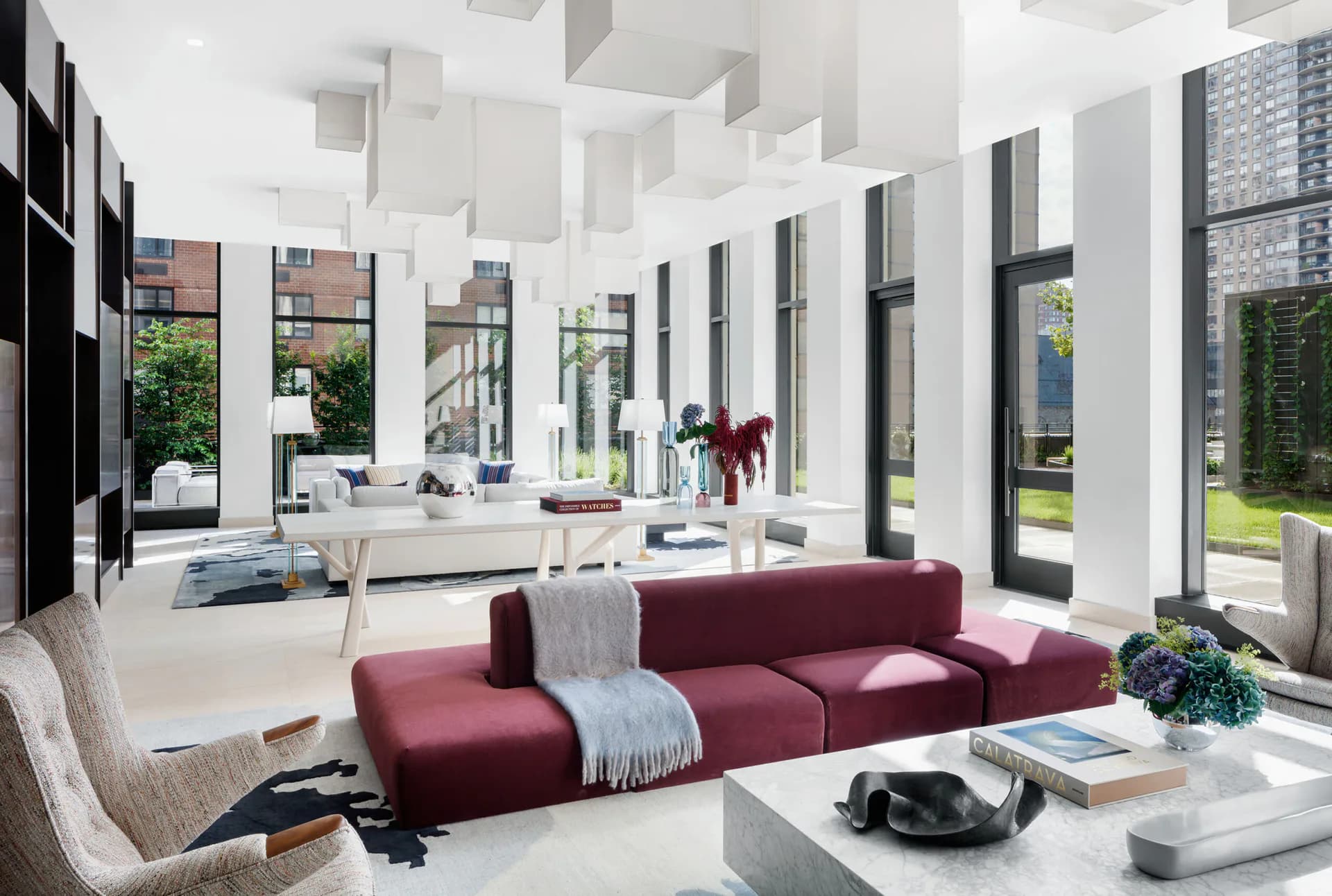 Bright modern living space with burgundy modular sofa, white cabinetry, extensive glass doors overlooking landscape, and minimalist furnishings by Pembrooke & Ives.