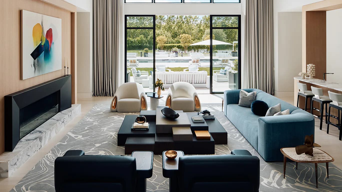 Modern living room with blue sofa, black ottomans, marble flooring, linear fireplace, and expansive glass doors opening to waterfront views by Pembrooke & Ives.