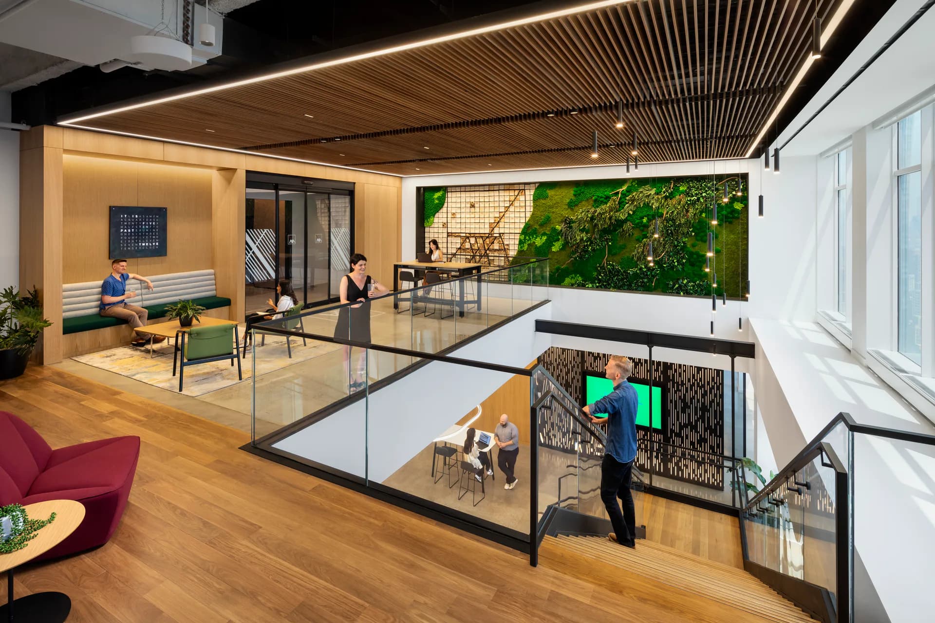 Multi-level office interior with wooden ceilings, glass partitions, green wall installation, and warm lighting designed by Perkins Eastman.