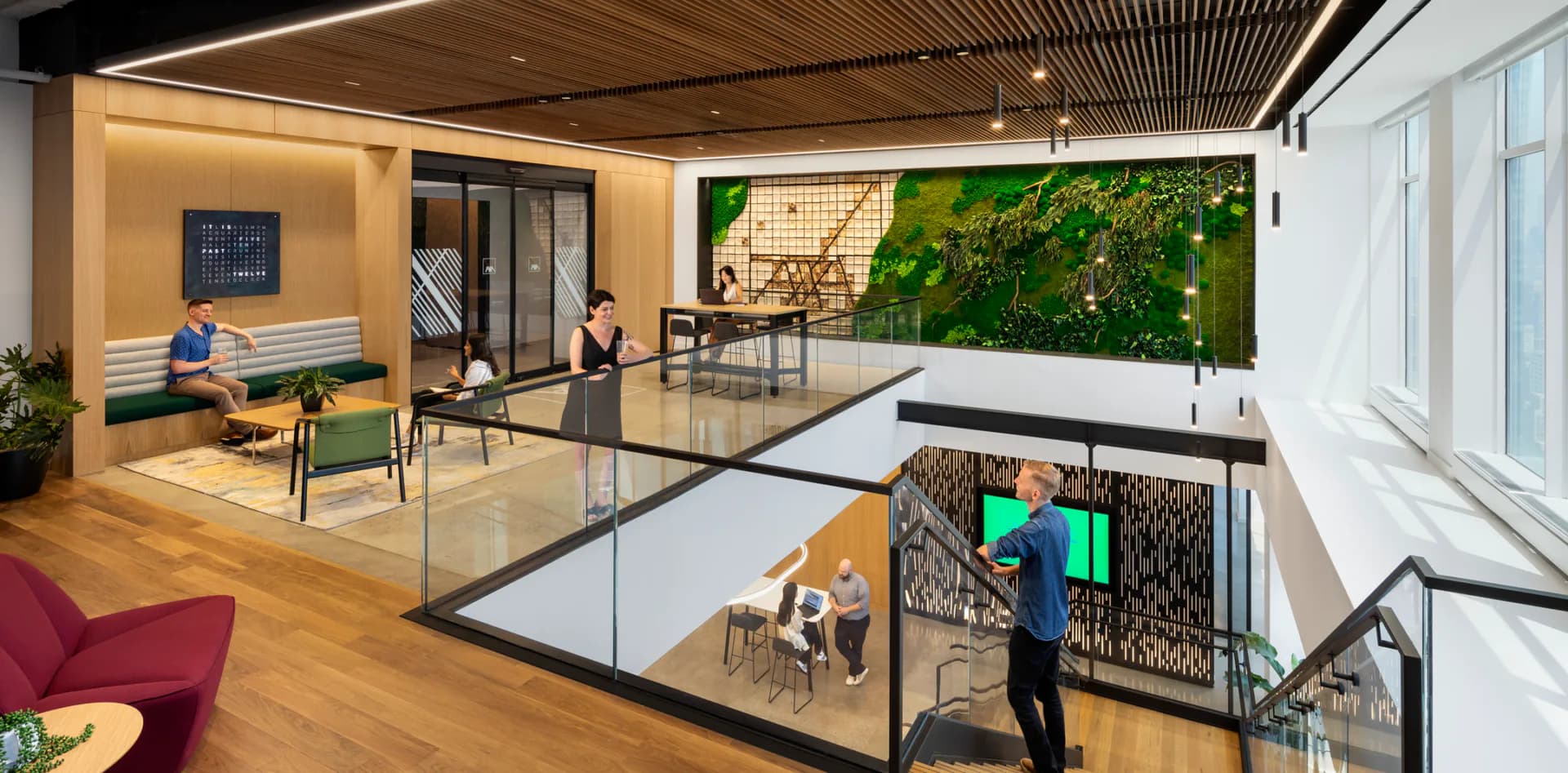 Multi-level modern office interior with warm wood ceilings, open collaborative spaces, green living wall, and natural light from floor-to-ceiling windows by Perkins Eastman.