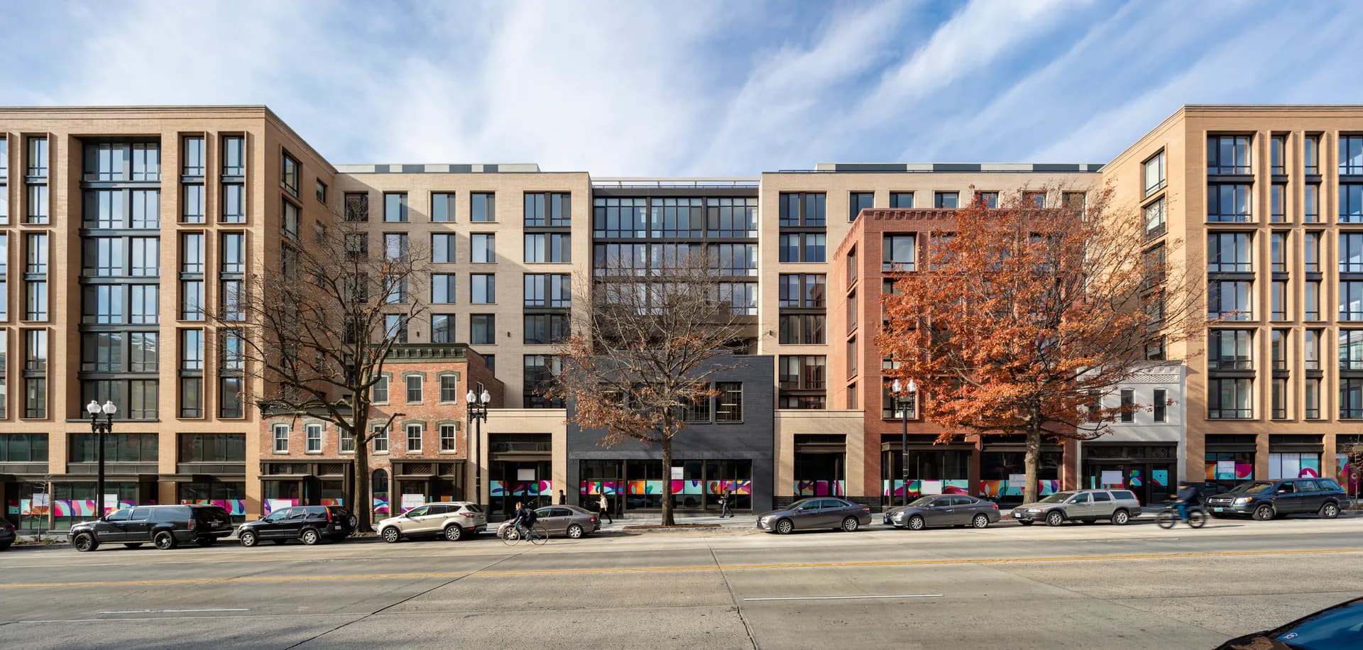 Modern mixed-use building facade with warm-toned brick and large windows, street-level retail spaces, and residential units above, designed by Perkins Eastman.