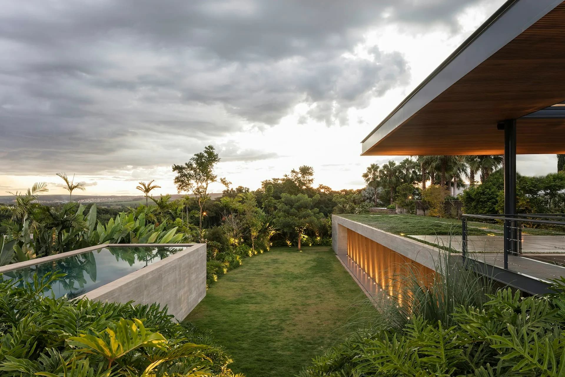 Modern residential landscape with curved pool, manicured lawn, tropical plantings, and contemporary architecture overlooking expansive views by Perkins&Will.