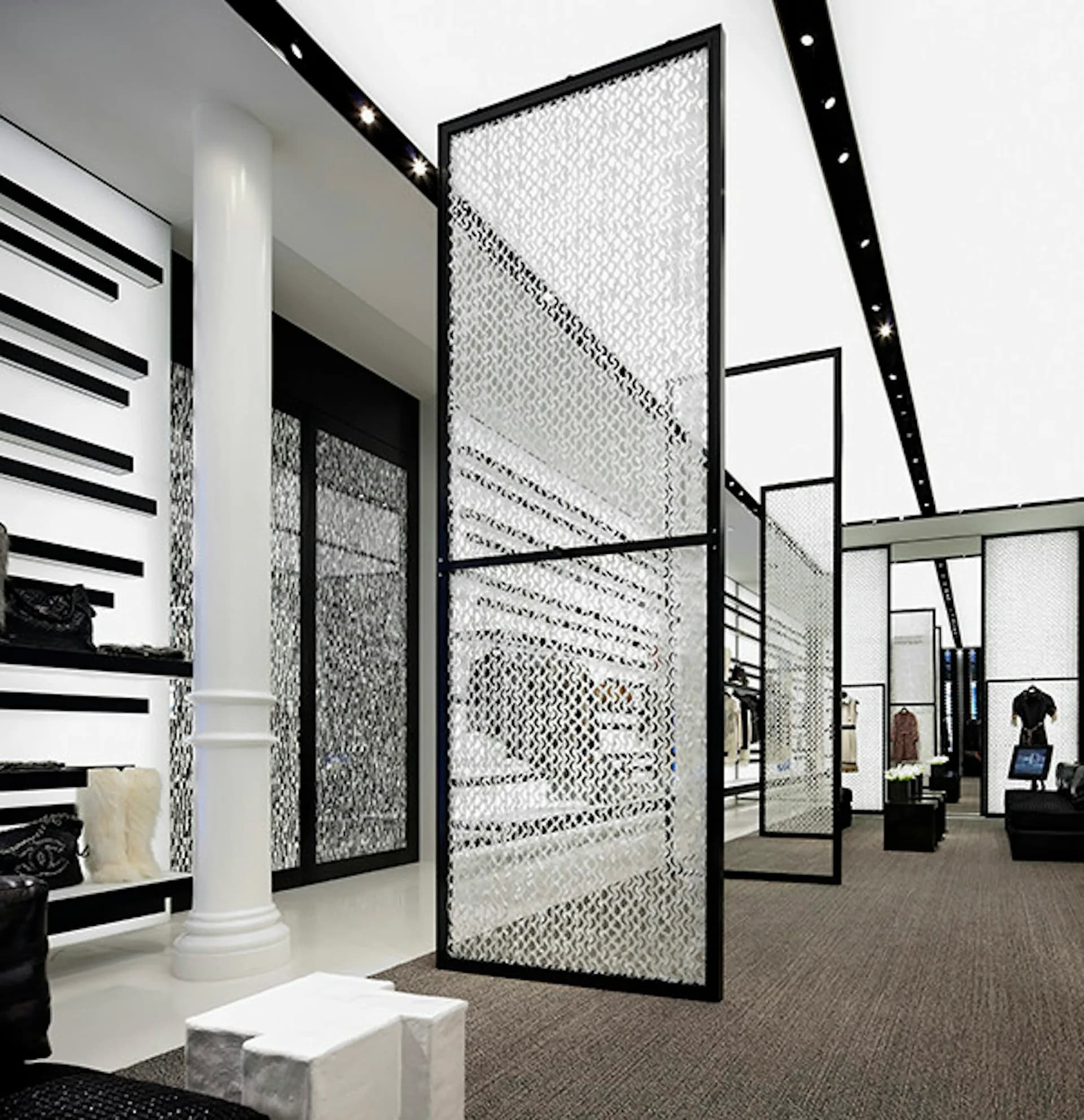 Modern retail showroom with black-framed perforated metal partitions, white columns, and polished concrete flooring by Peter Marino Architect.