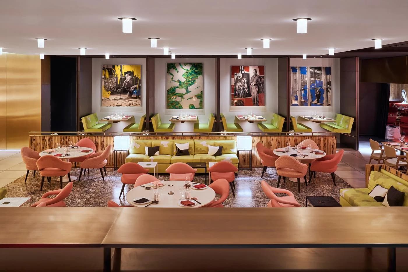 A luxury restaurant dining room with terracotta-upholstered chairs, sage green accents, and warm wood tones, featuring abstract artwork and contemporary lighting by Peter Marino Architect.