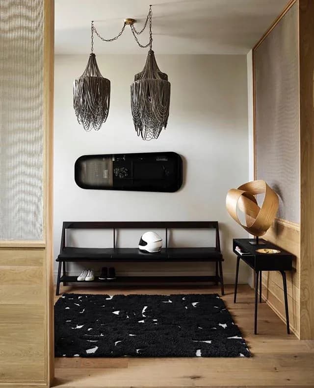Modern entryway with black bench, tassel pendant lights, sculptural wood sphere, and geometric patterned rug by Phaedo Design.