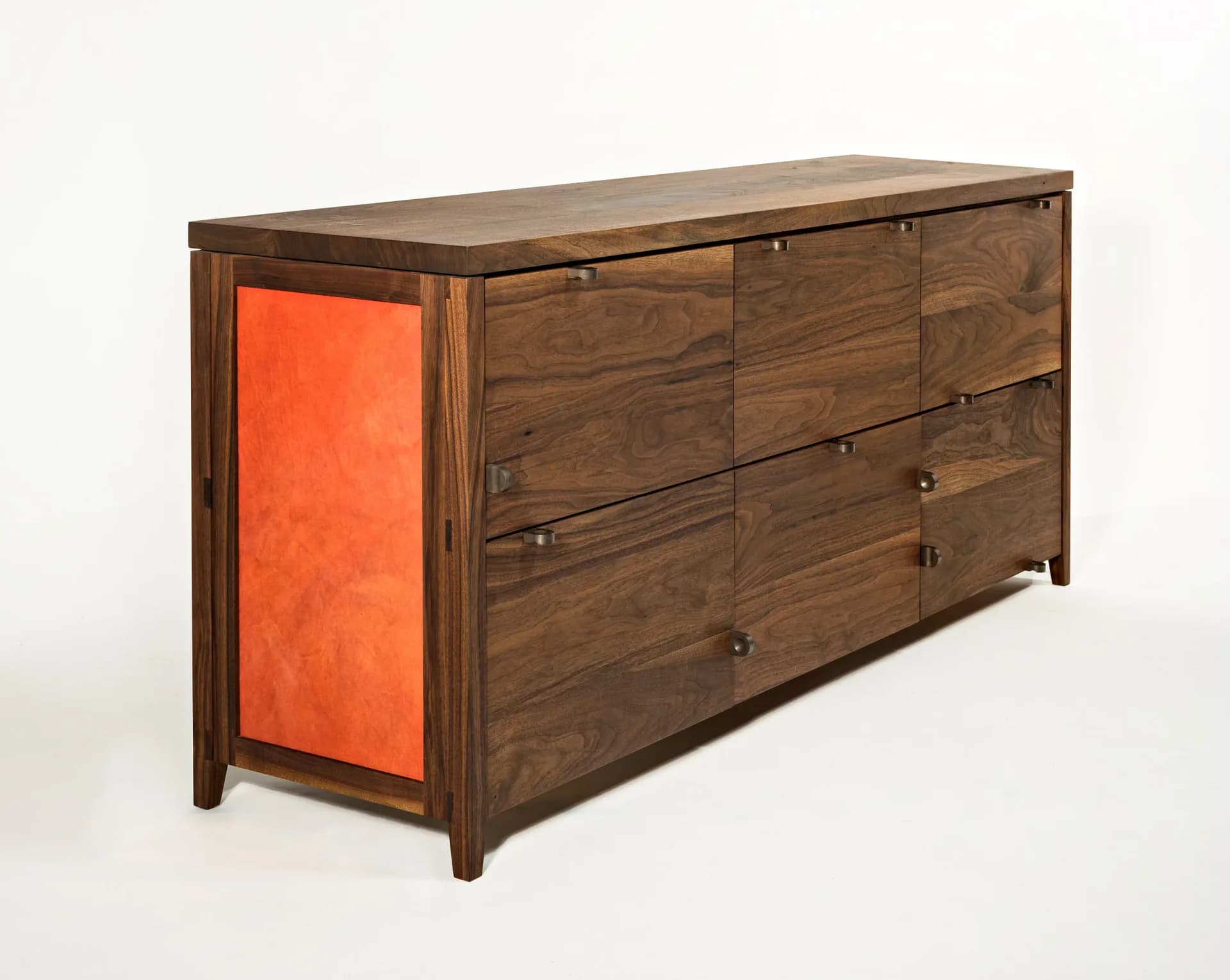 Walnut dresser with six drawers and orange-upholstered left panel, featuring clean lines and metal hardware, by Phaedo Design.