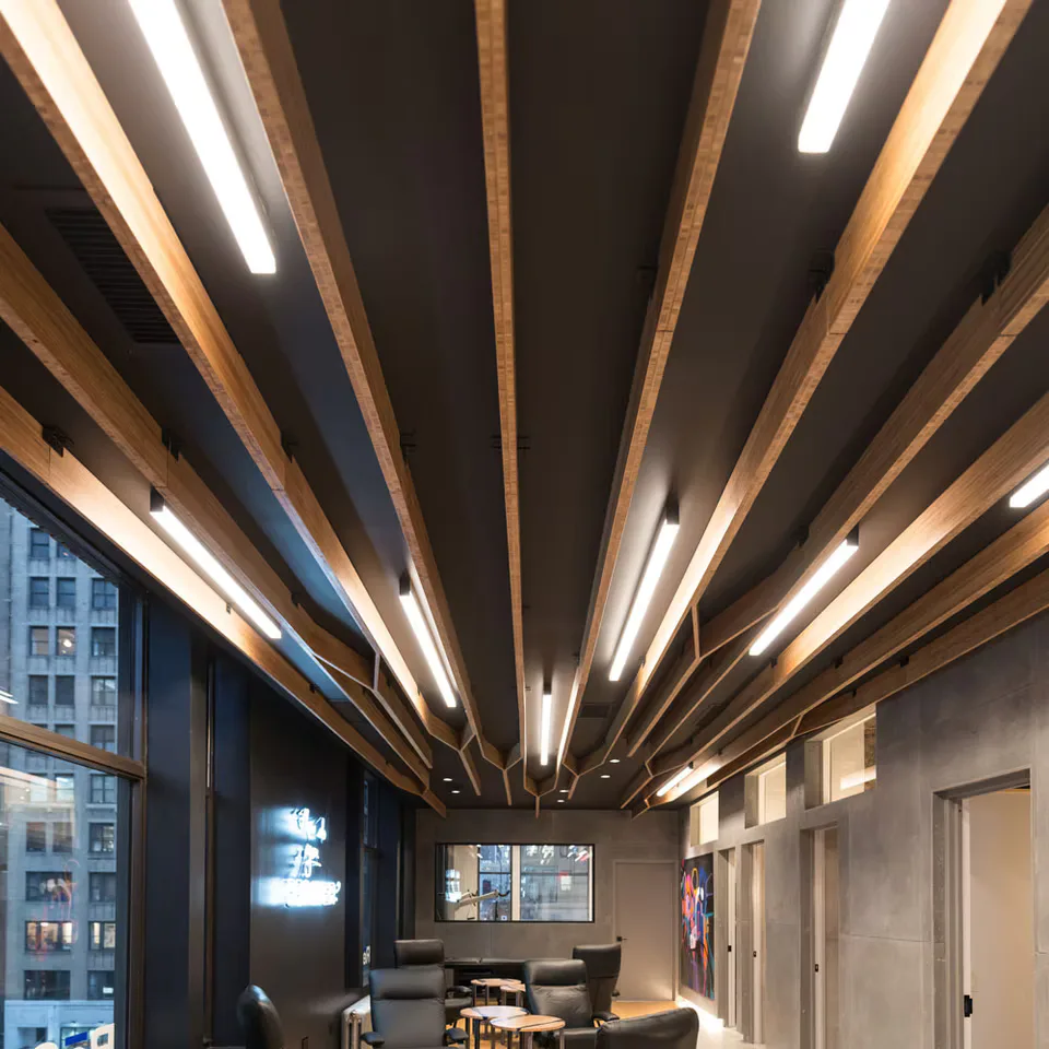 Modern corridor with radiating wood-slat ceiling featuring integrated linear LED lighting creating dramatic geometric patterns, contemporary office or hospitality space by PHT Lighting Design.