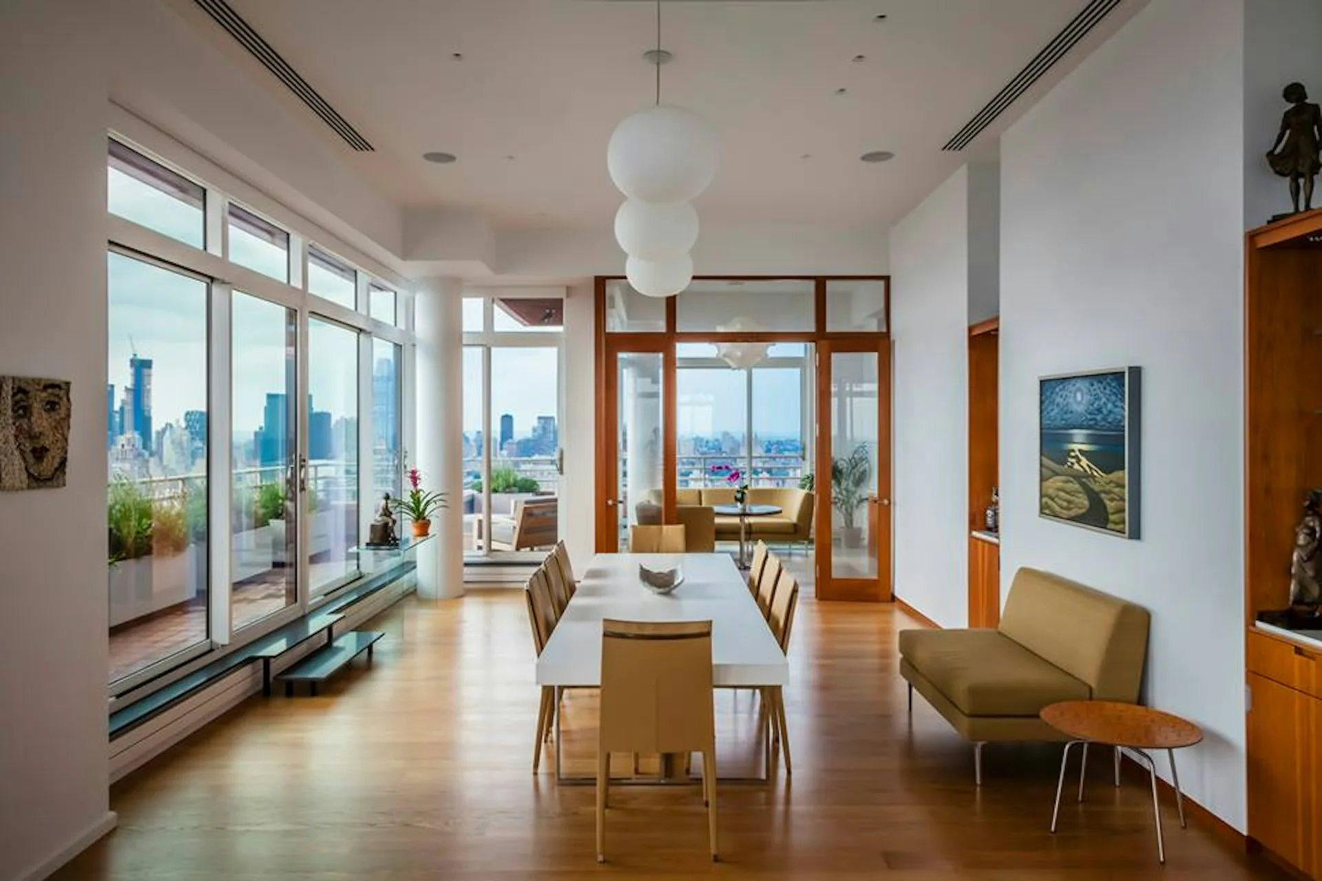 Modern dining room with wood floors, mid-century furniture, and expansive windows overlooking a city skyline by Pier, Fine Associates.