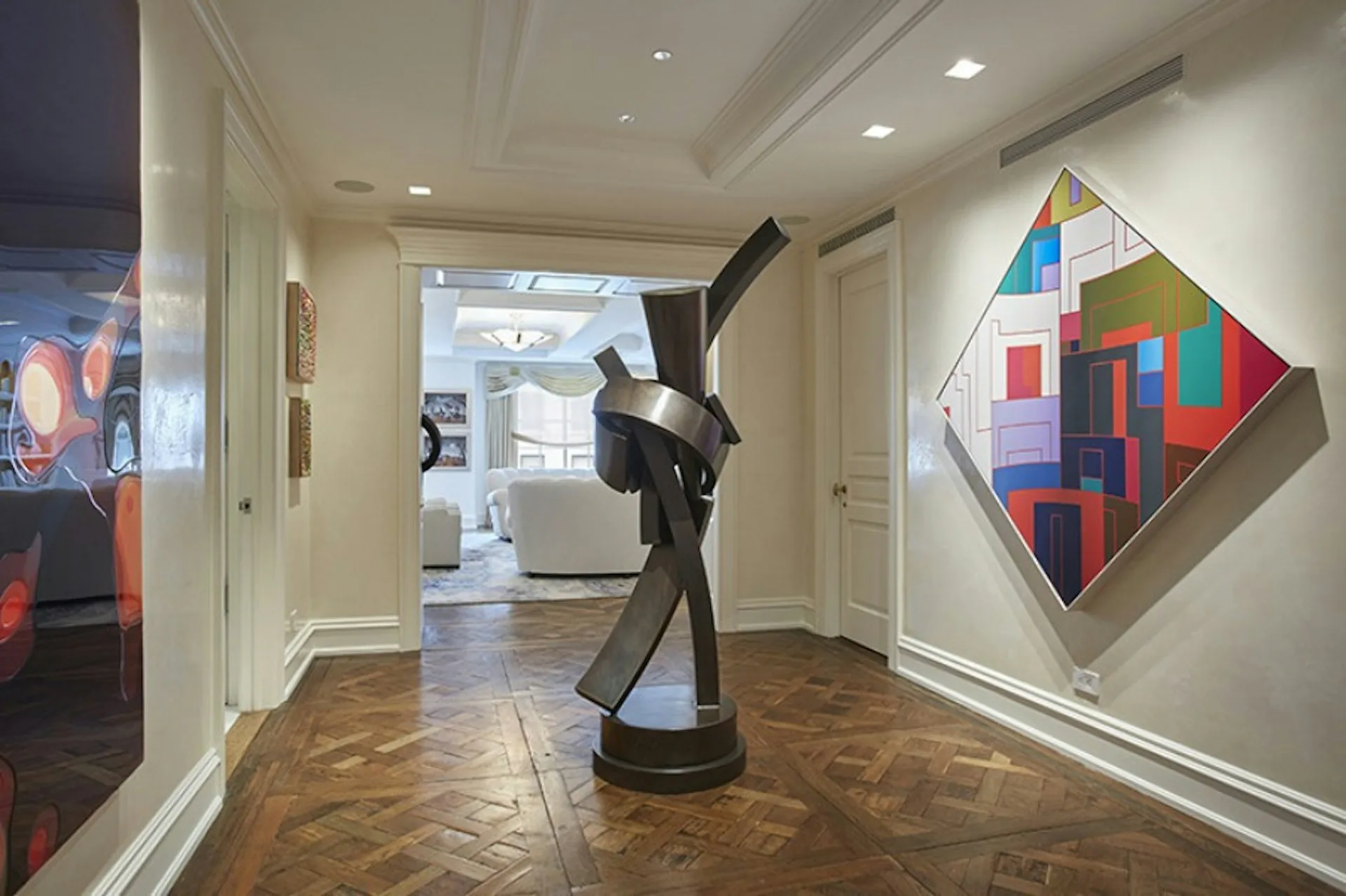 Contemporary gallery space with herringbone wood flooring, coffered ceiling, featuring a black sculptural figure and colorful abstract geometric artwork on white walls, designed by Pier, Fine Associates.