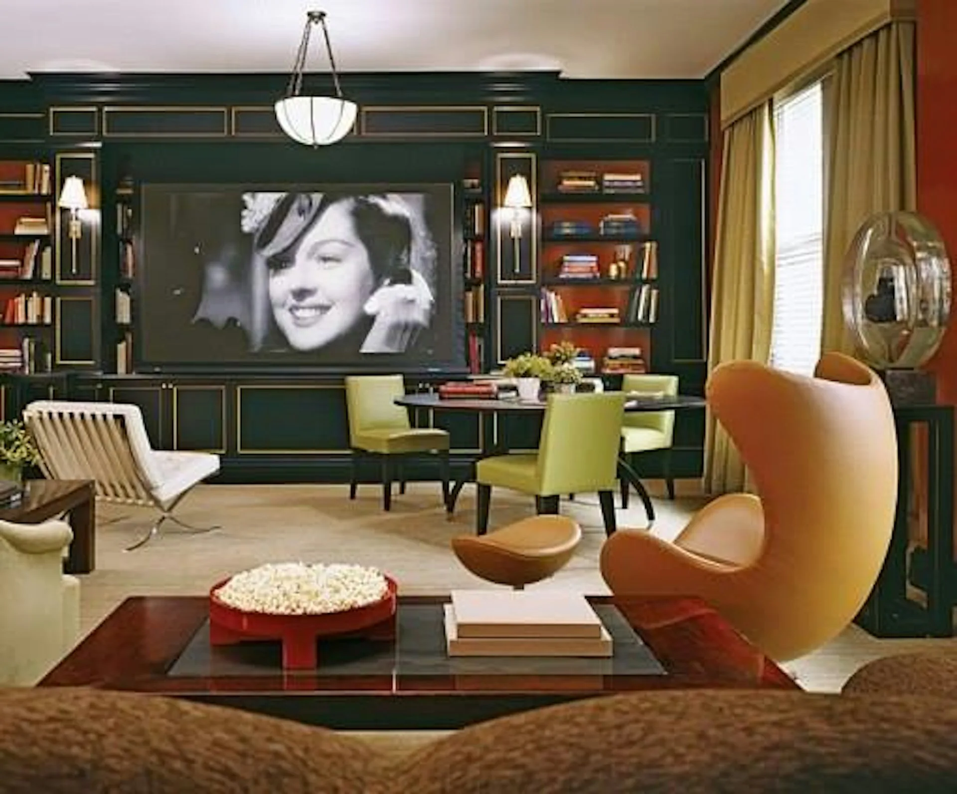 Modern media room with deep forest-green paneled walls, vintage furnishings in mustard and cognac tones, and a floating shelving unit displaying books by Pier, Fine Associates.