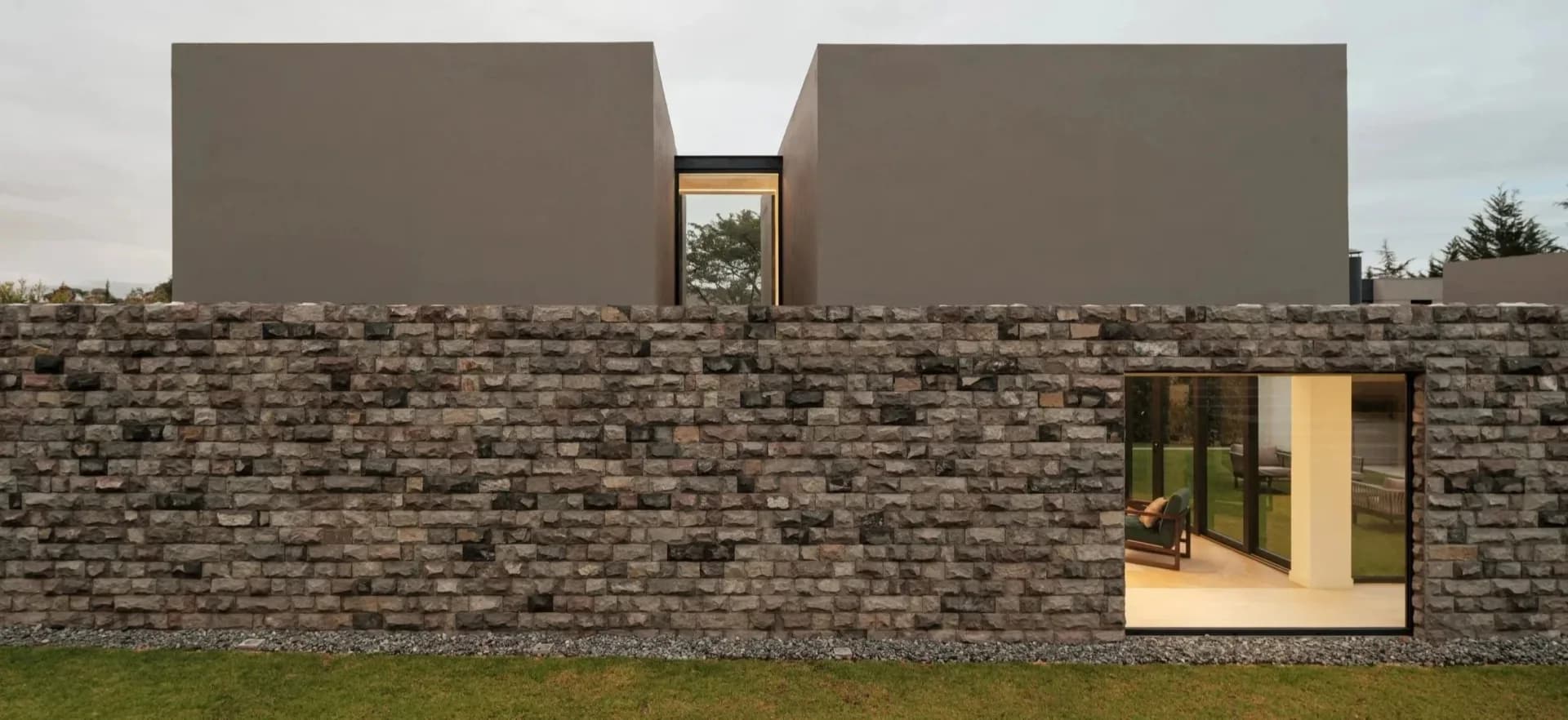 Modern stone brick building with two concrete volumes and a central window opening, featuring minimalist architectural design by PJCArchitecture.