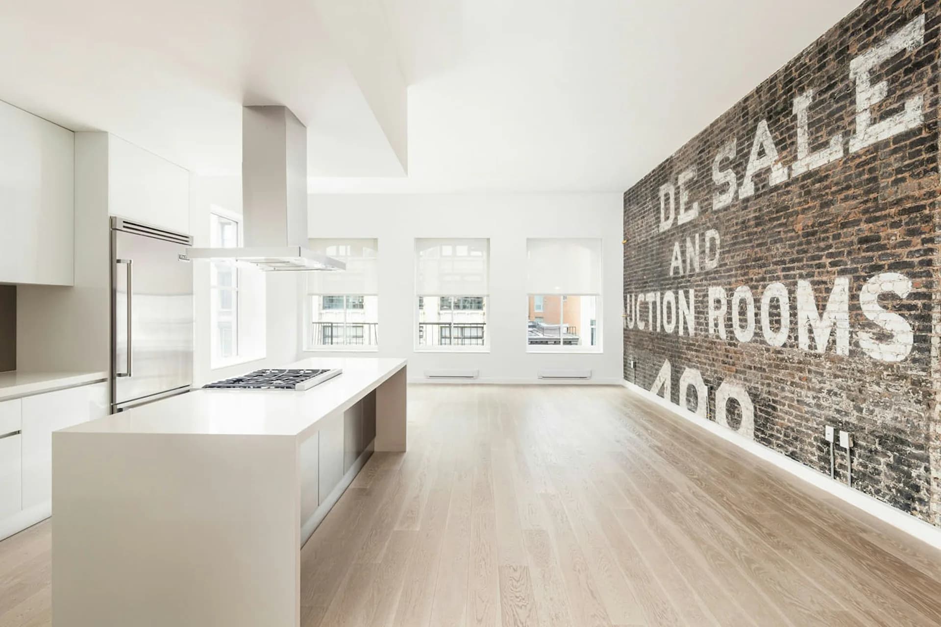 Modern loft kitchen with white cabinetry, island, and exposed brick wall featuring vintage signage, designed by PKSB Architects.