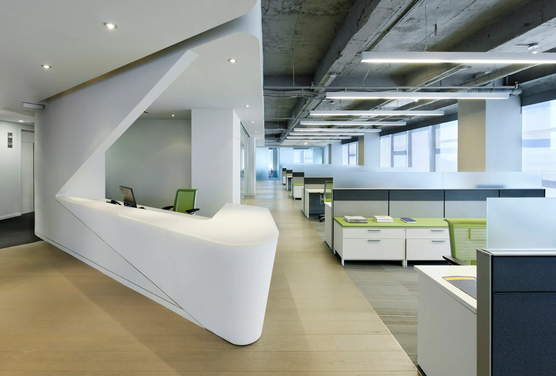 Modern office reception area with curved white desk, green accent seating, exposed concrete ceiling, and warm wood flooring designed by PKSB Architects.