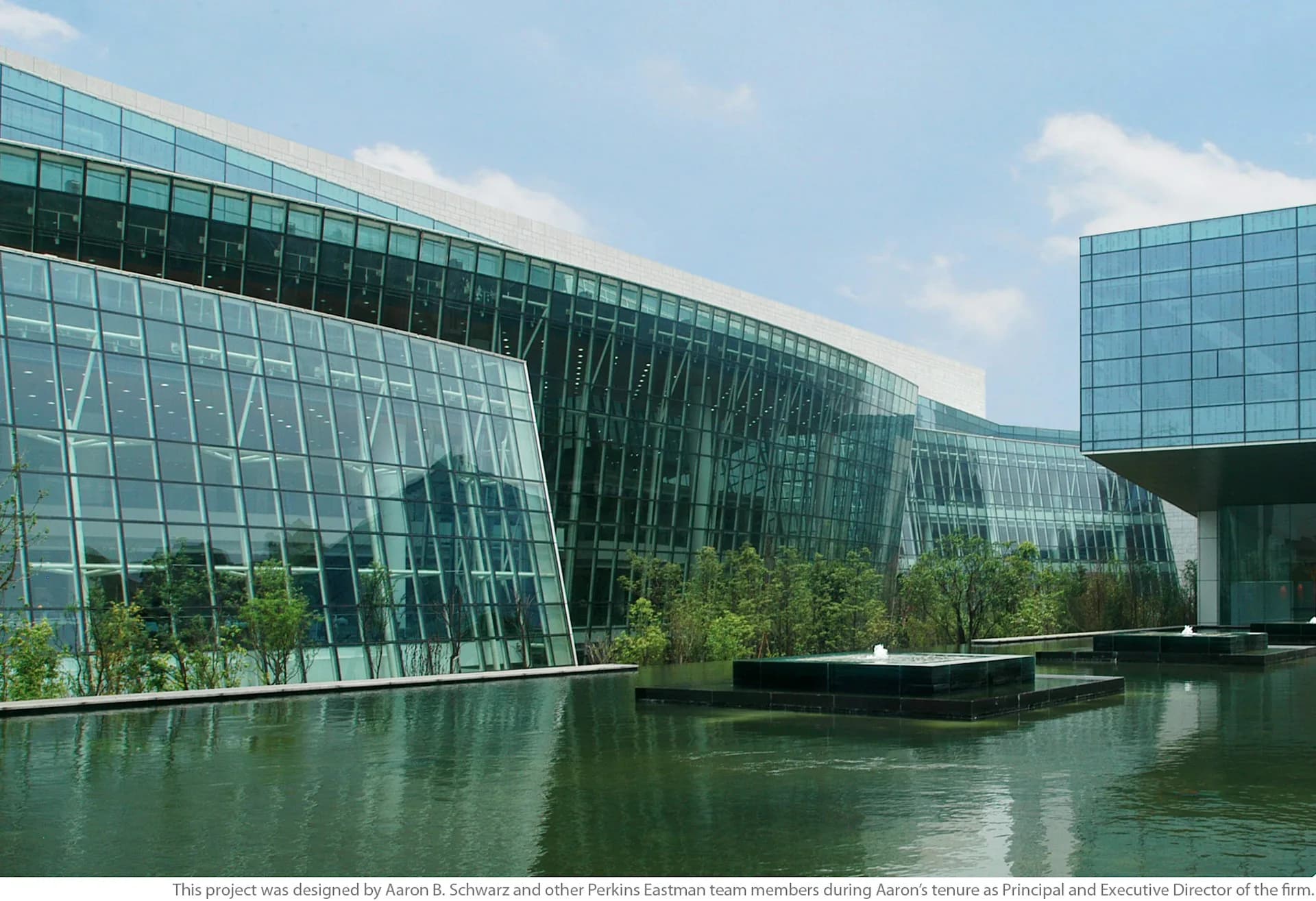 Modern glass and steel waterfront building with curved facades reflected in still water, surrounded by green landscape by Plan A.