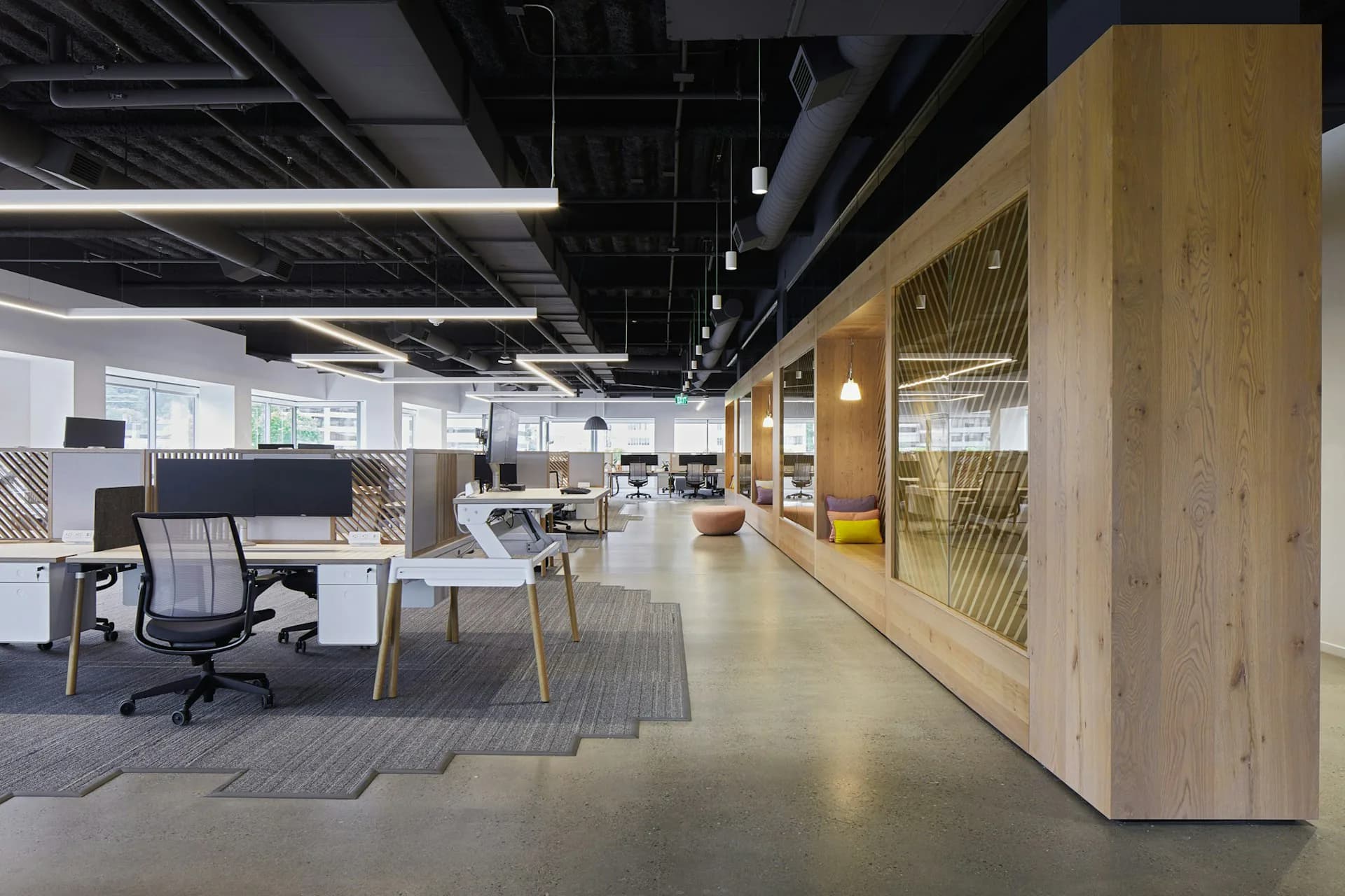 Modern open-plan office space featuring natural wood millwork, polished concrete floors, and contemporary workstations with grey seating by Pliskin Architecture PLLC.