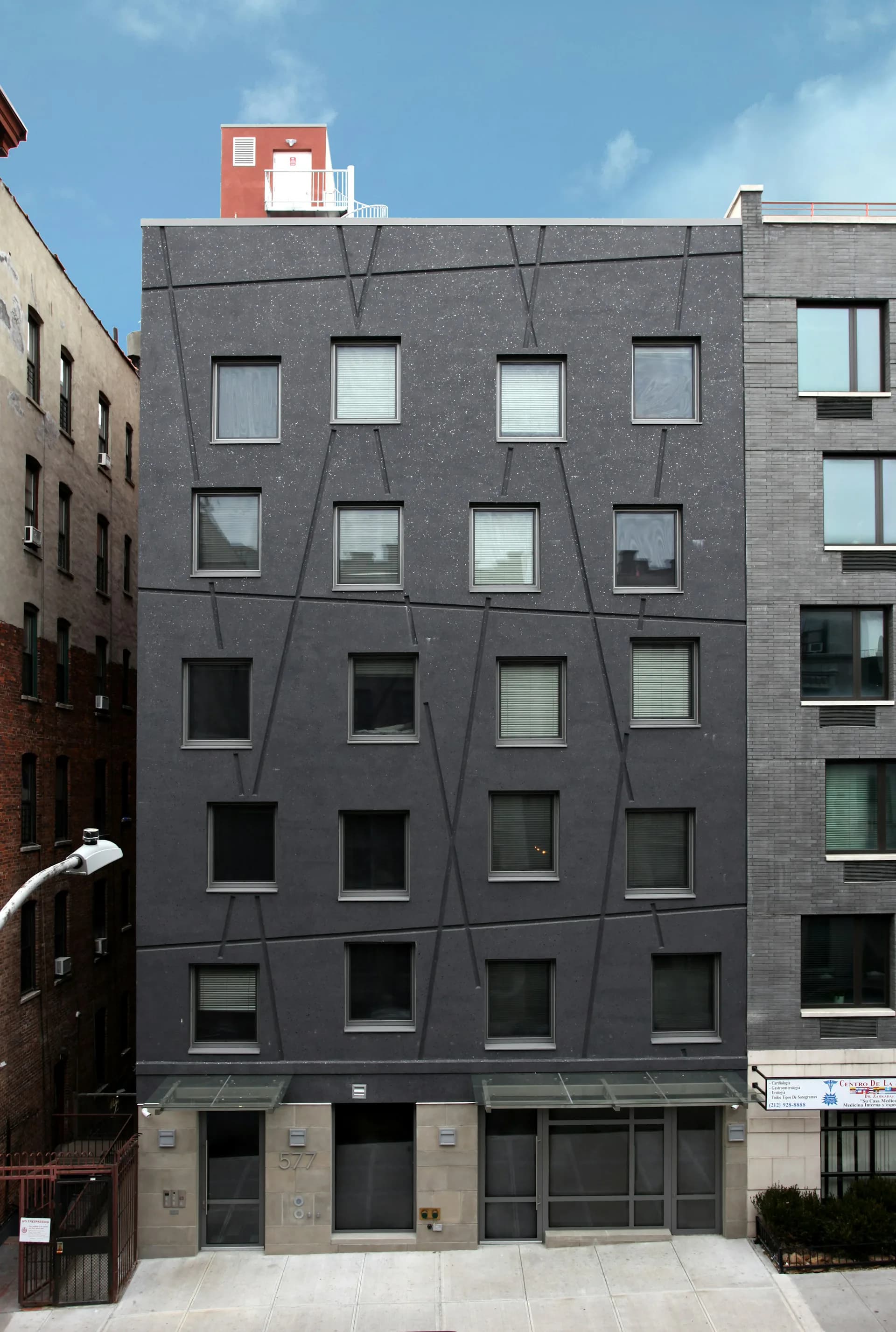 Dark gray contemporary residential building facade with geometric window pattern and ground-floor retail space, designed by PM Architecture PC.