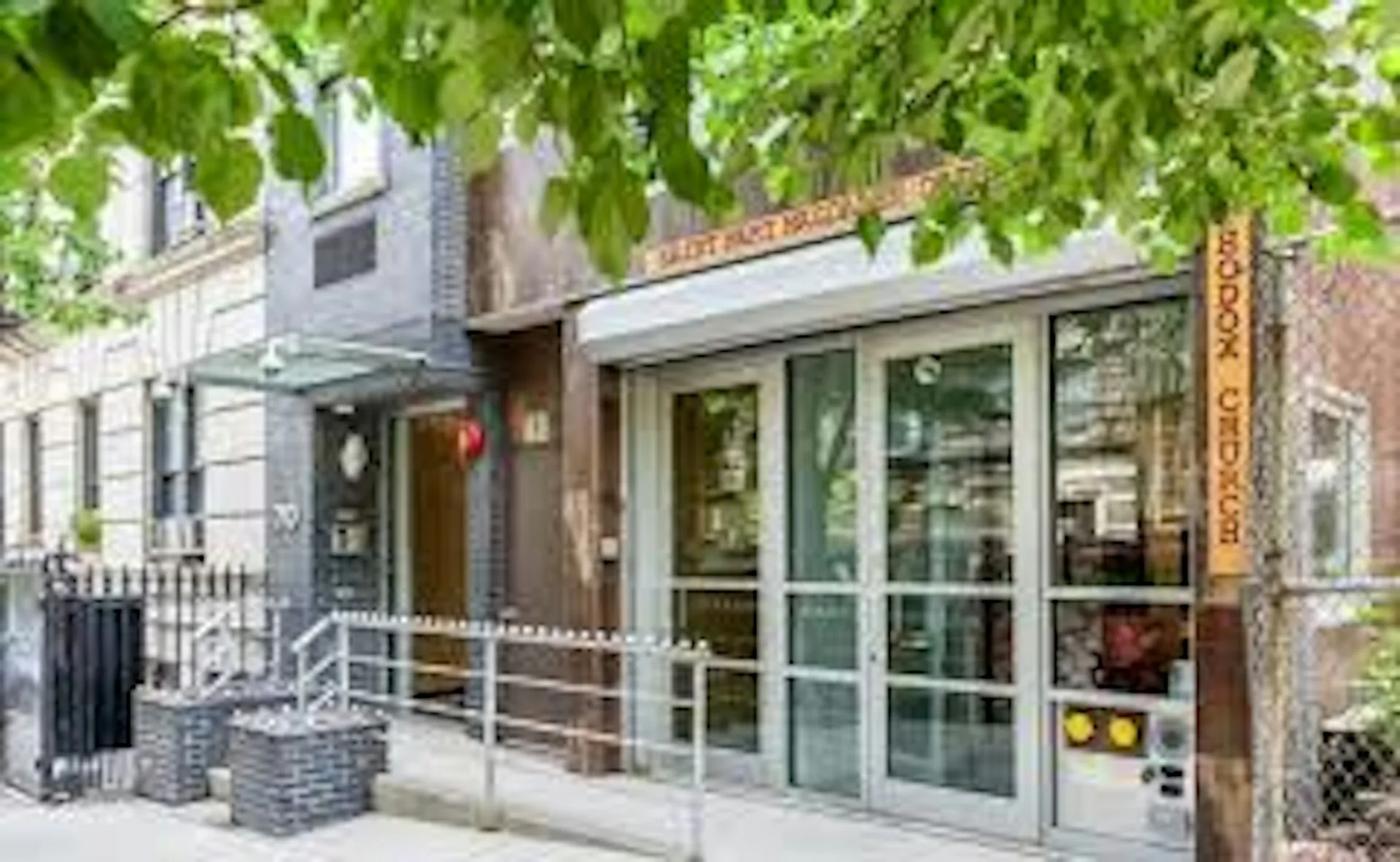 Street-facing storefront with floor-to-ceiling glass doors, brick and metal facade, and green awning, featuring modern commercial design by PM Architecture PC.