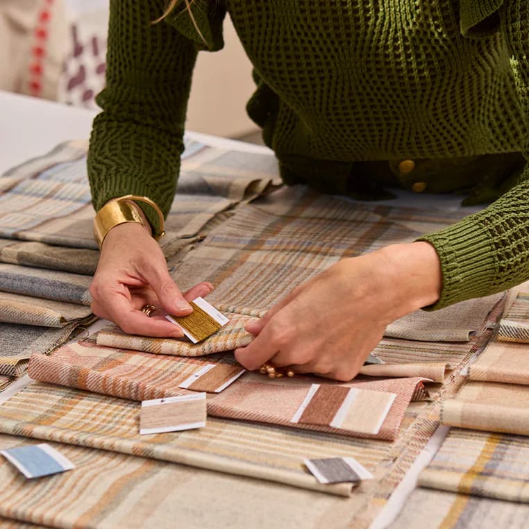 Designer's hands selecting fabric swatches in neutral tones with striped patterns arranged on a table by Pollack.