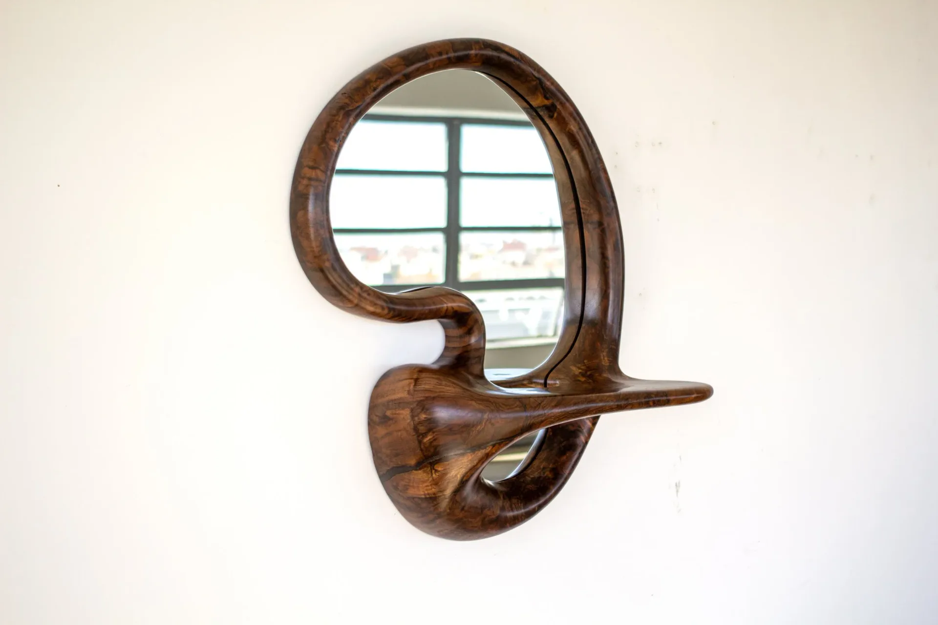 Sculptural wooden mirror with organic curved forms and warm walnut finish mounted on white wall by Poritz & Studio.