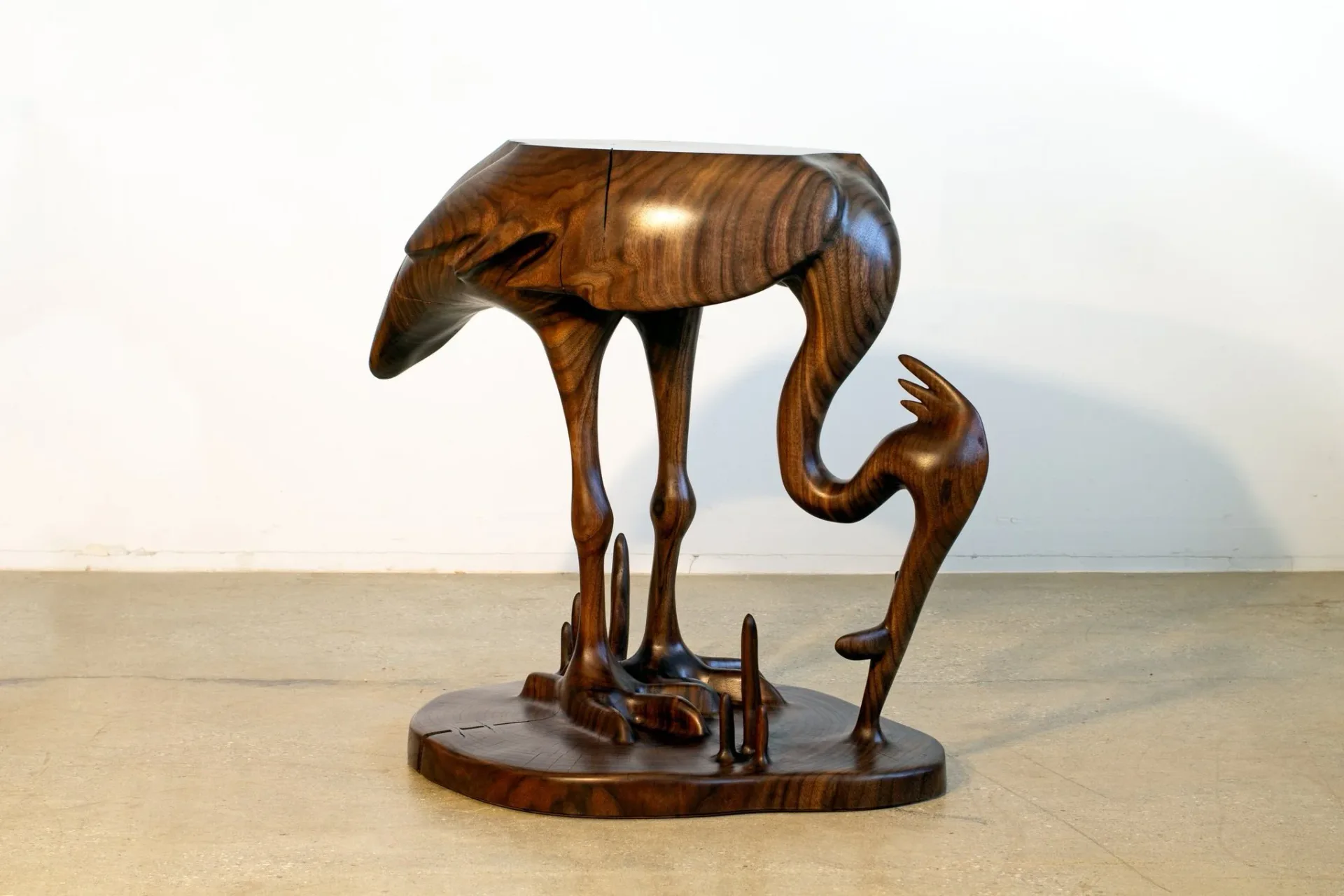 Wooden sculptural installation featuring a stylized animal figure with elongated legs on a circular base, carved from rich brown wood by Poritz & Studio.