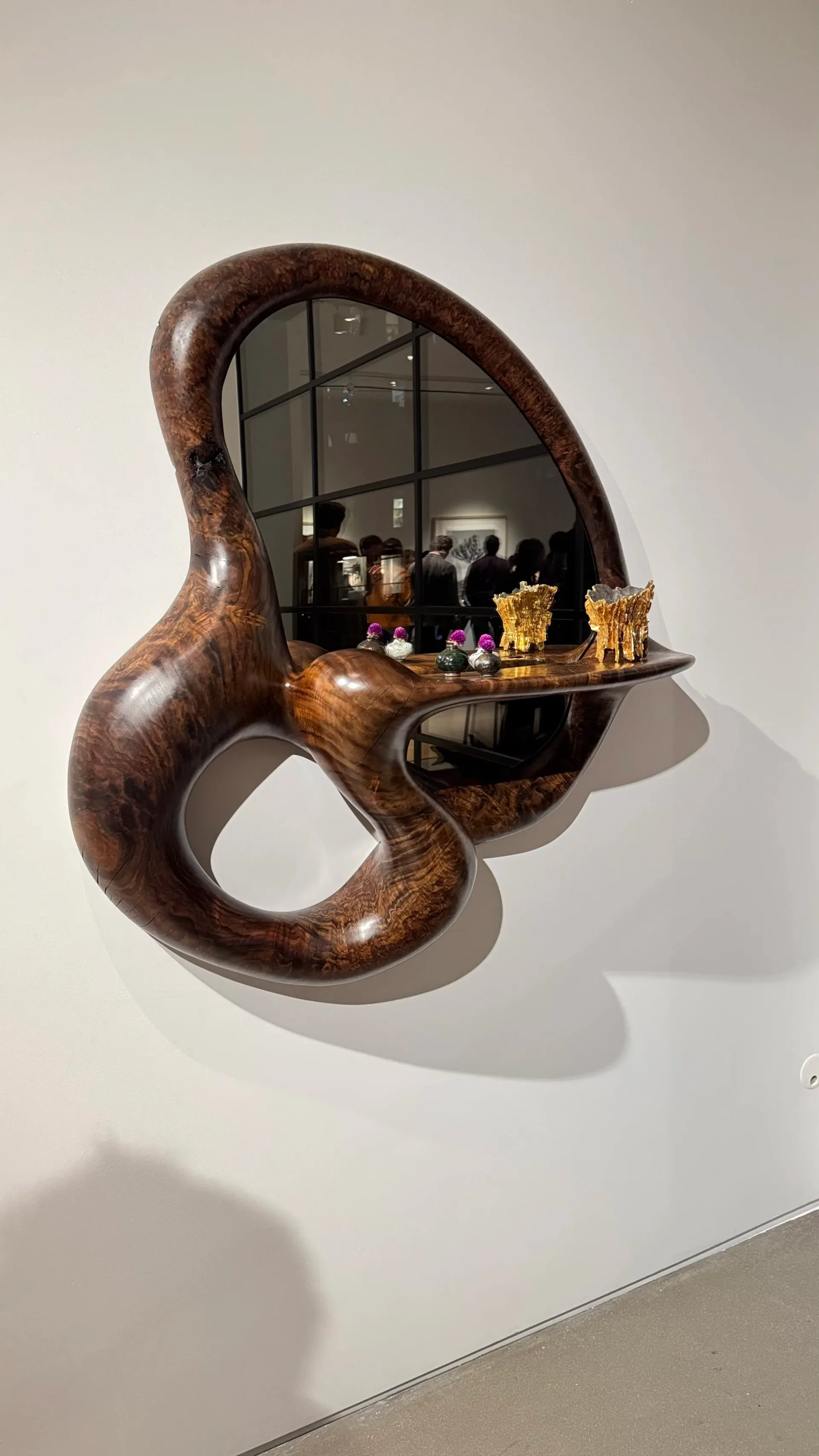 Sculptural wooden wall installation with organic curved forms, mirrored interior, and brass shelf displaying objects, by Poritz & Studio.