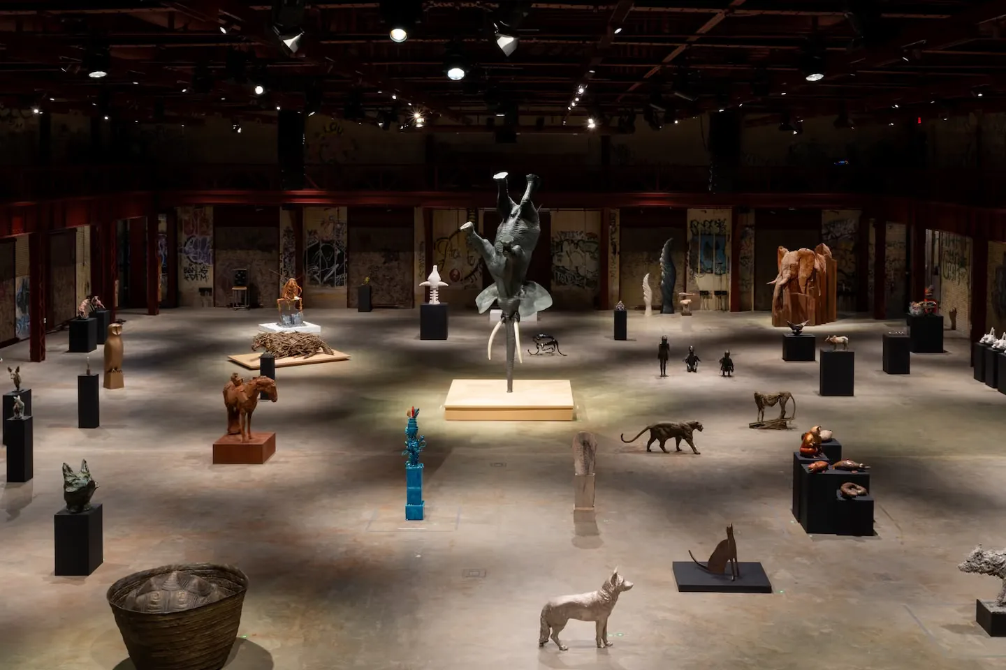 A large gallery space with concrete floors displays sculptural artworks and installations on pedestals under warm accent lighting, designed by Powerhouse Arts.