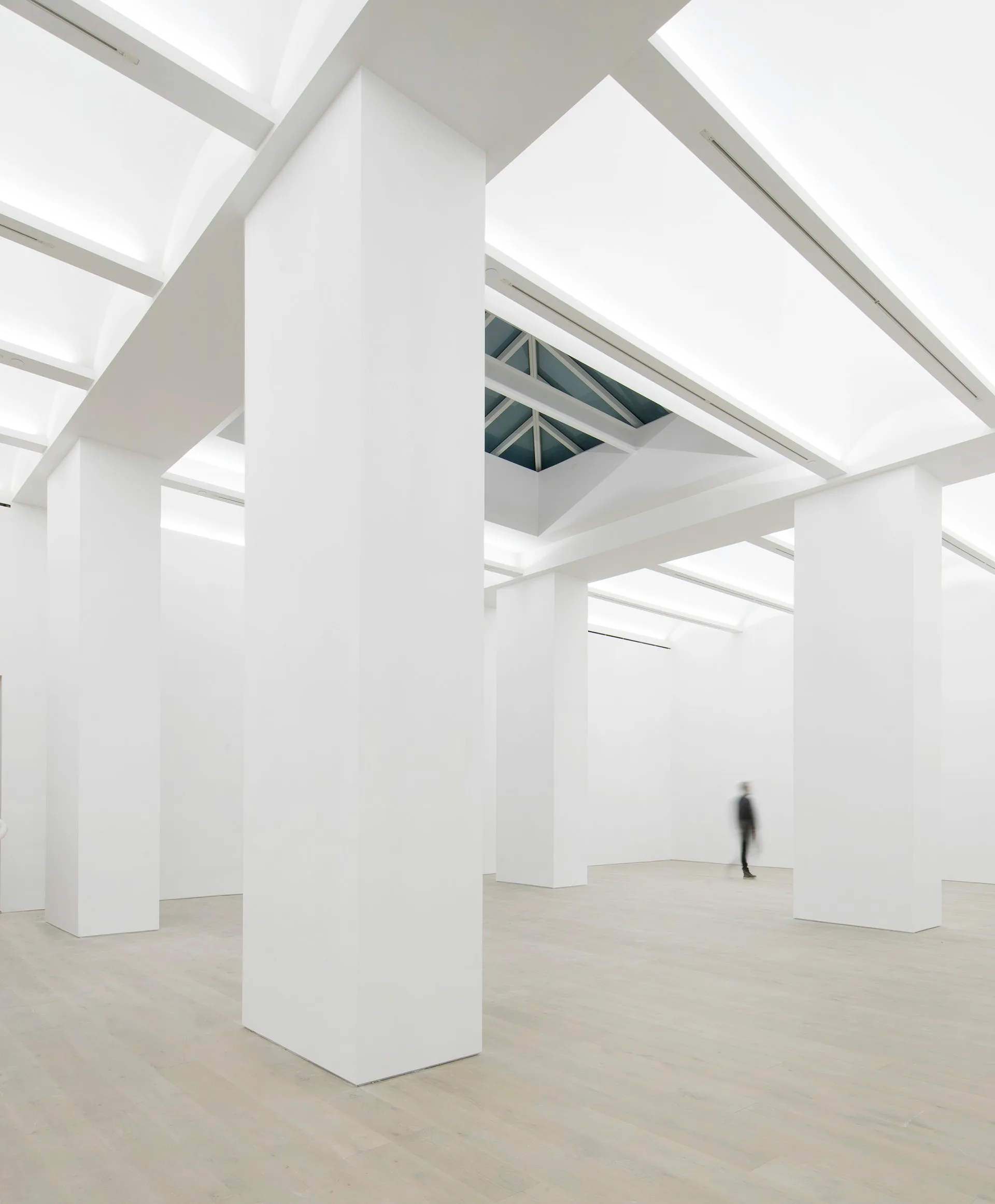Minimalist white interior with structural columns, skylights, and polished concrete floor, creating a clean gallery-like space by P.R.O. - Peterson Rich Office.