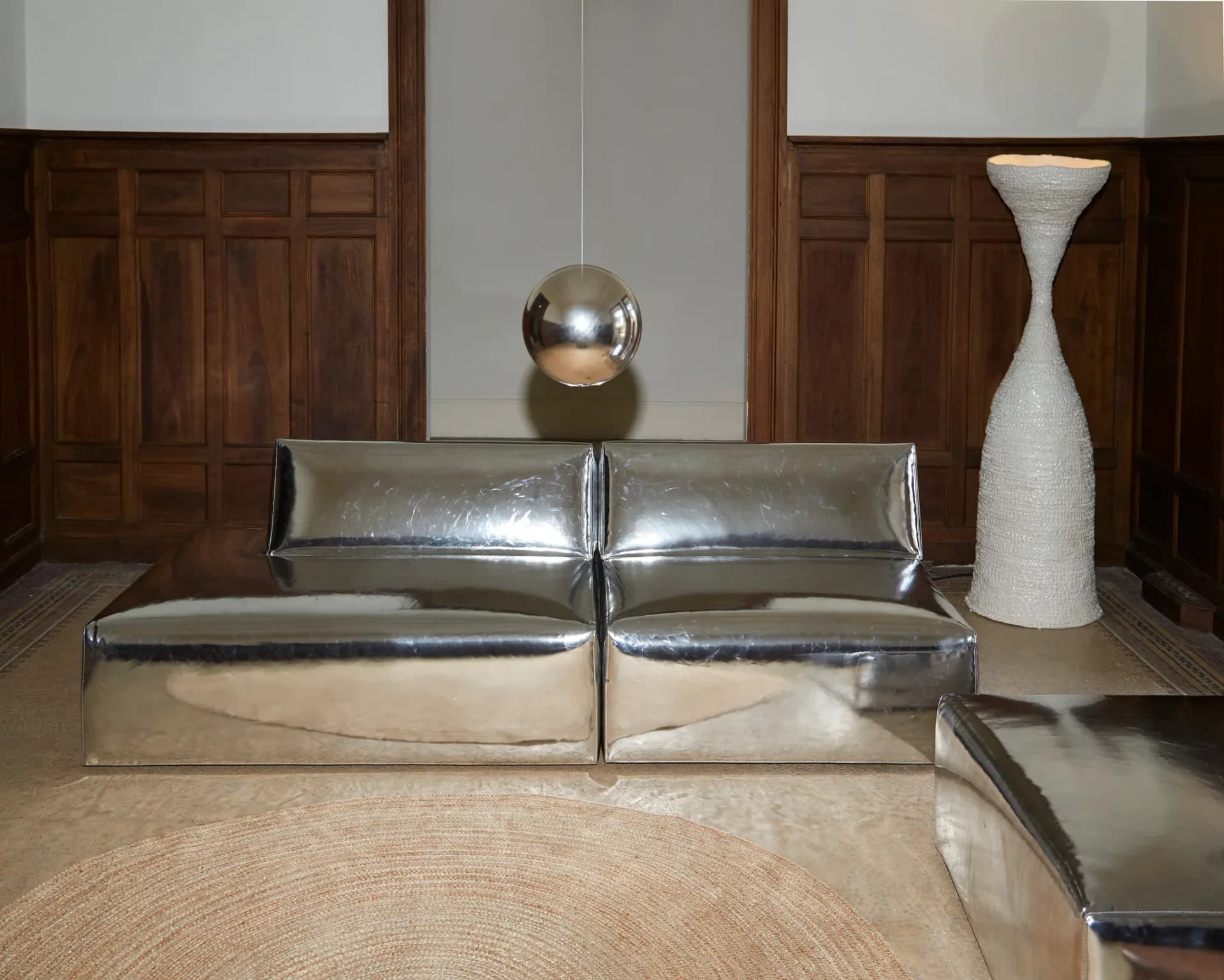 Minimalist interior with metallic leather seating, polished concrete floor, suspended chrome sphere, and white sculptural vase by Project 213A.