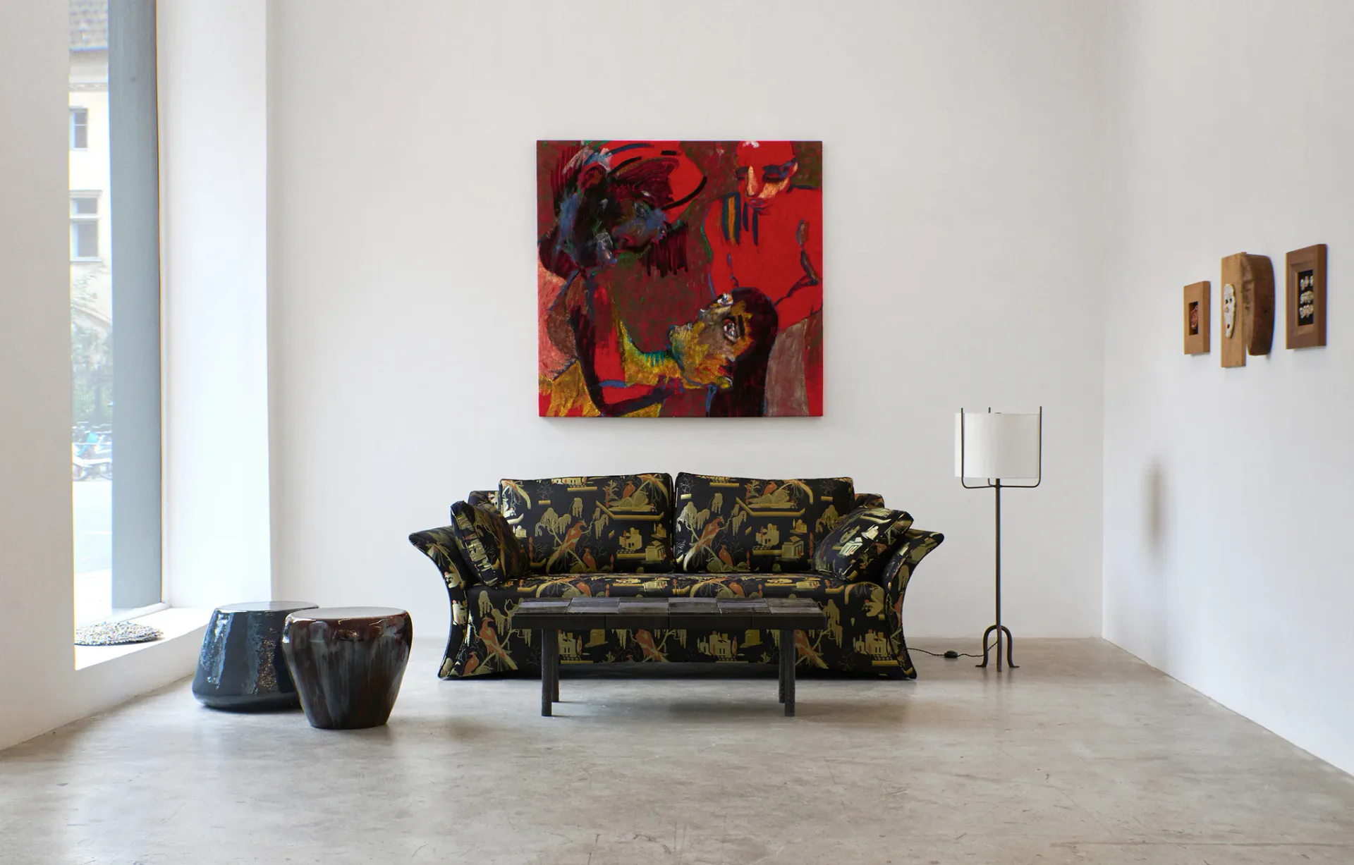 Minimalist gallery space with patterned sofa, red abstract artwork, small sculptural pieces, and polished concrete floor by Project 213A.