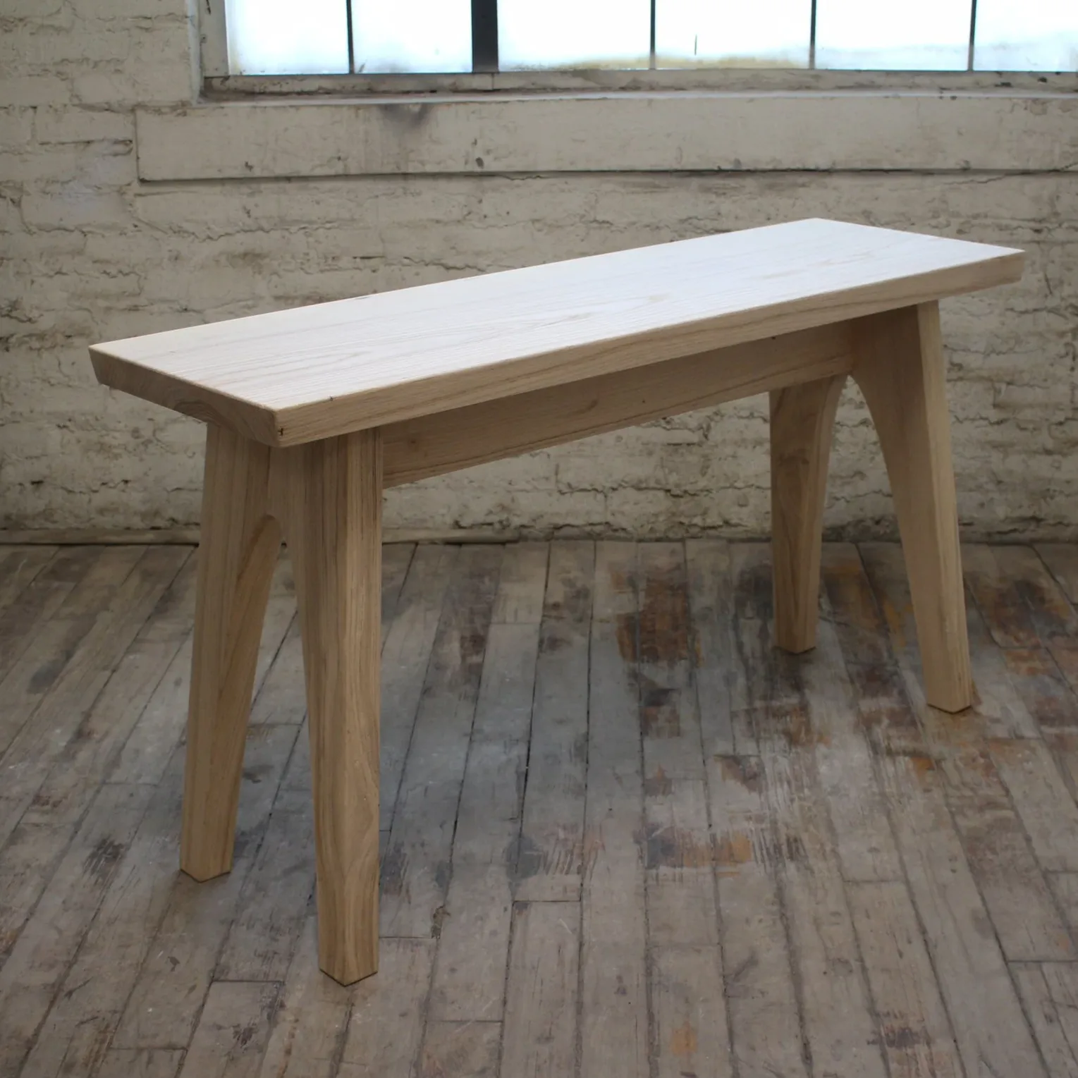 Light wood console table with clean lines and tapered legs displayed in an industrial loft space by Prospect Woodworks.