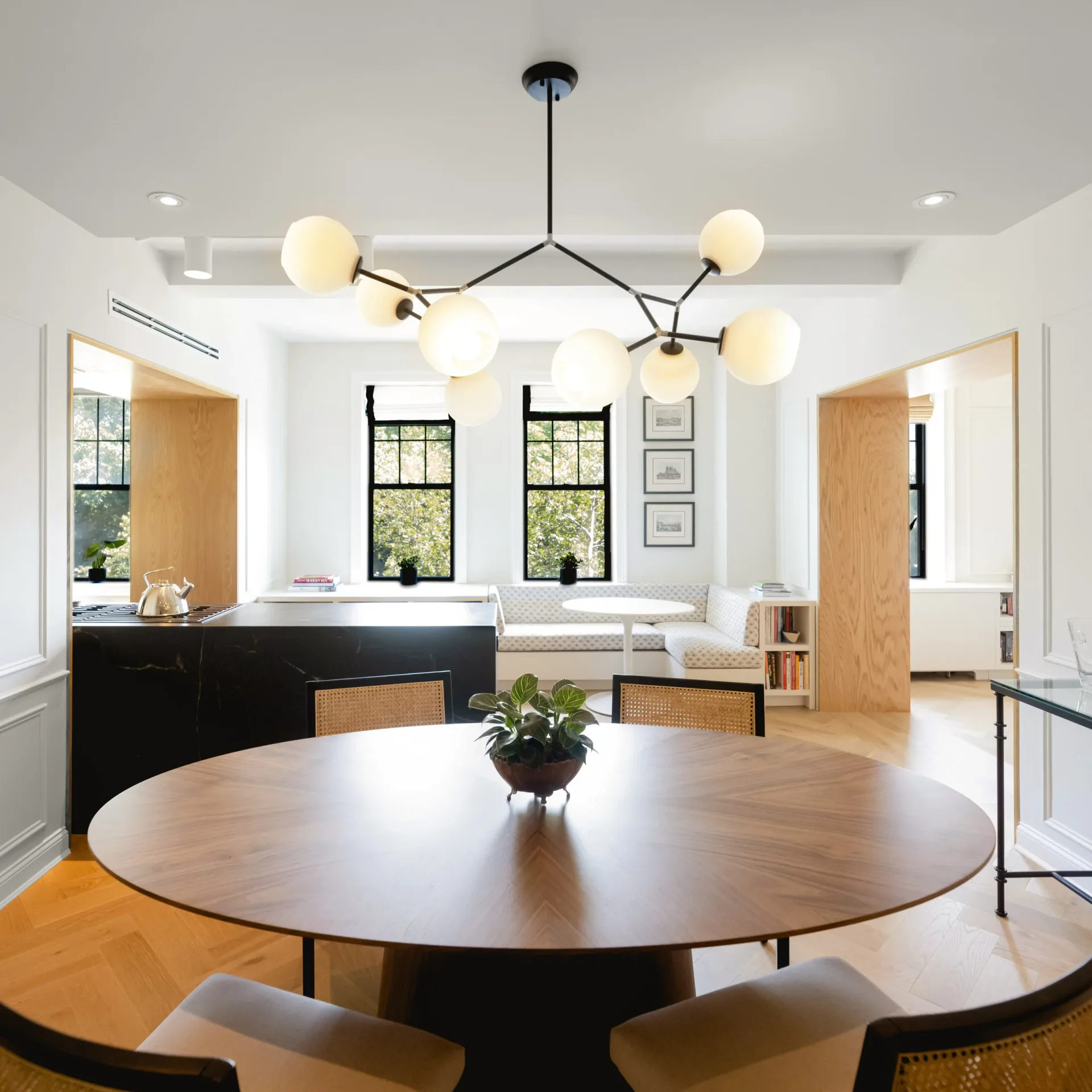 Modern dining room with round black table, natural wood chairs, cream pendant lighting, and wood-framed doors by Prospect Woodworks.