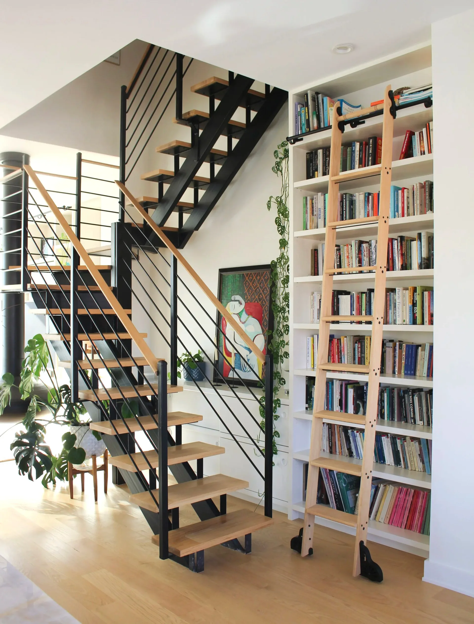 Modern staircase with black steel frame and wood treads beside a floor-to-ceiling bookshelf with wood frame by Prospect Woodworks.