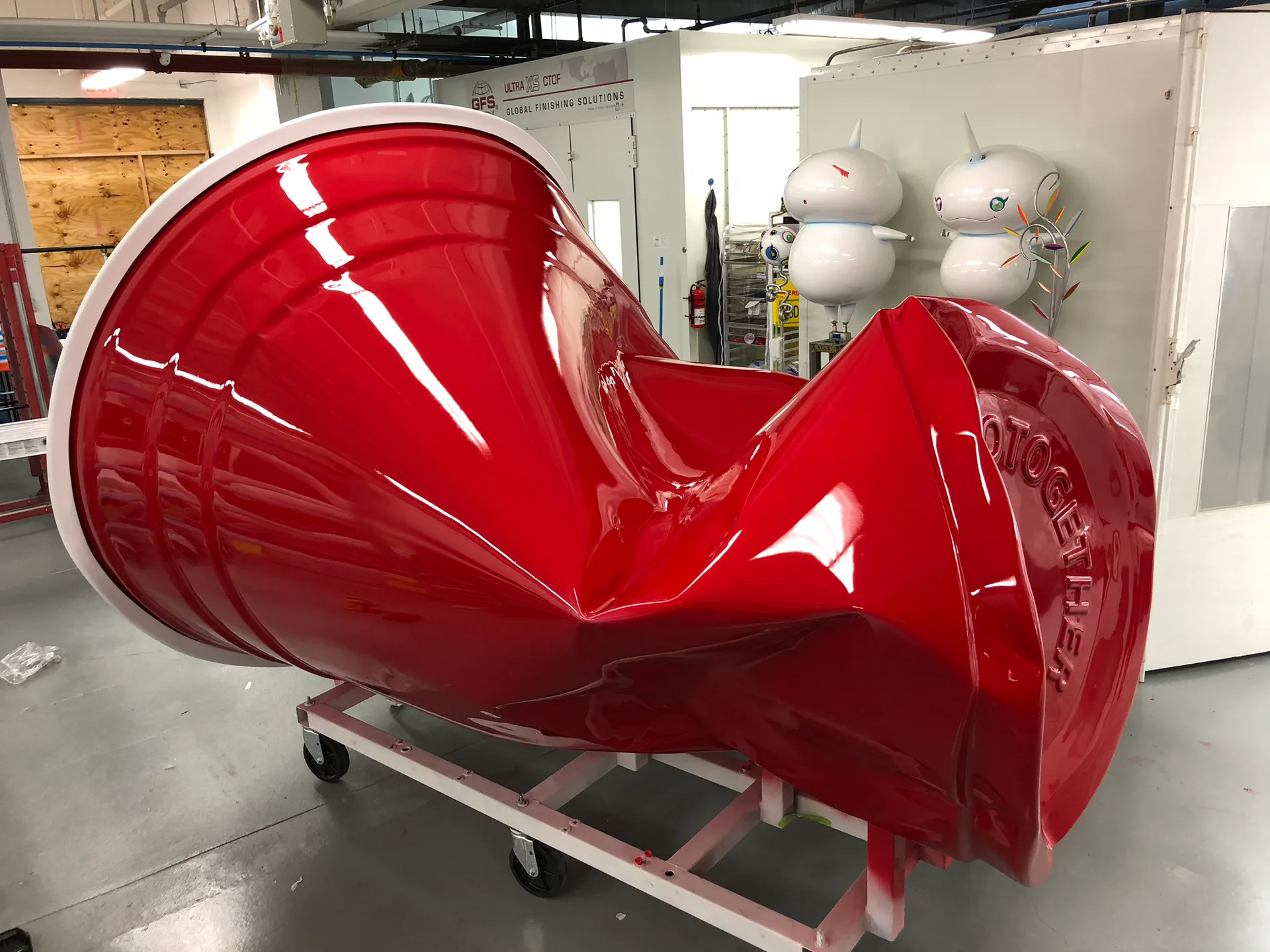 Glossy red sculptural form in industrial studio space, showcasing curved design and polished finish by Prototype New York.