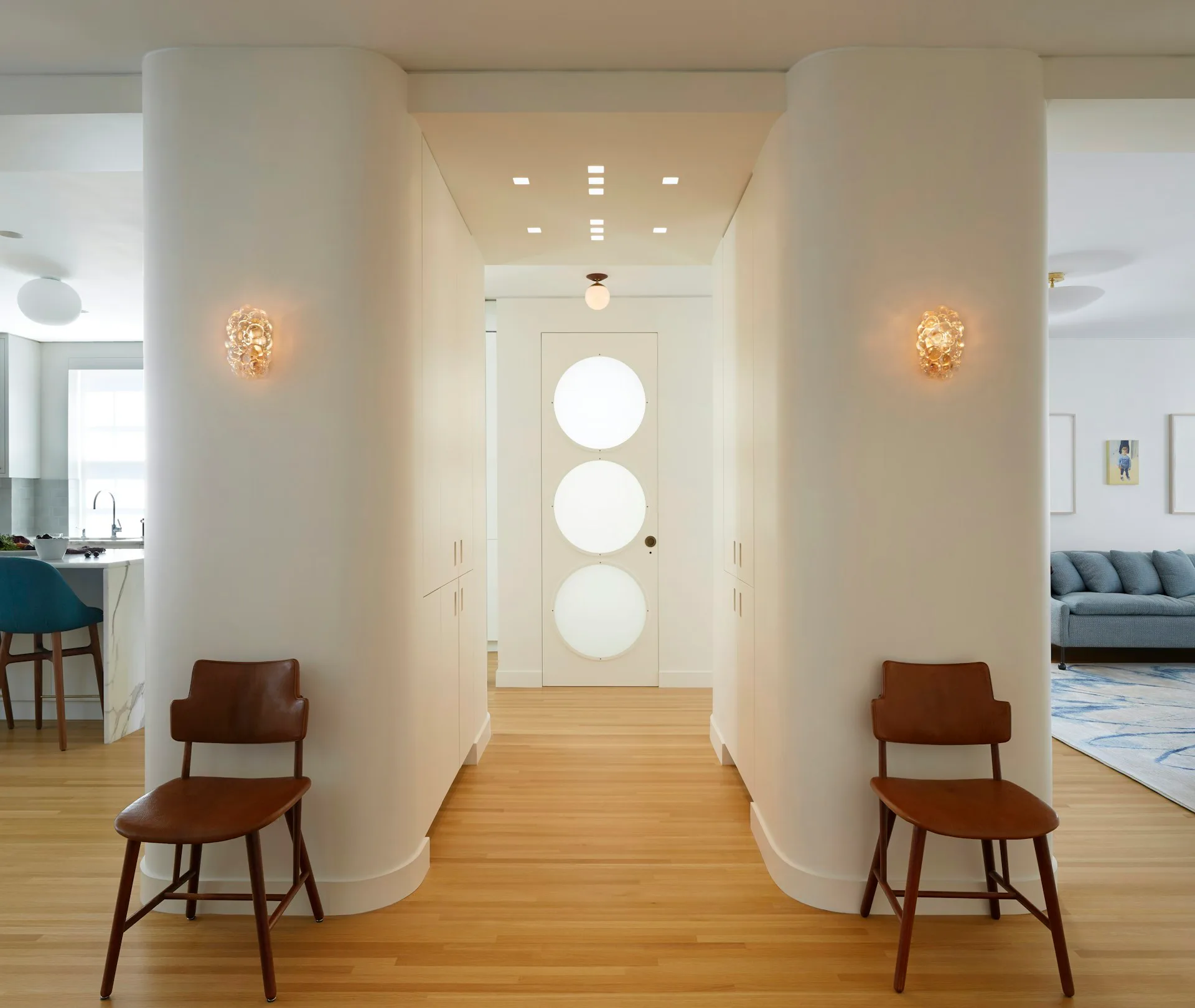 Minimalist hallway with curved white walls, wooden flooring, mid-century modern chairs, and circular window openings, designed by pulltab.